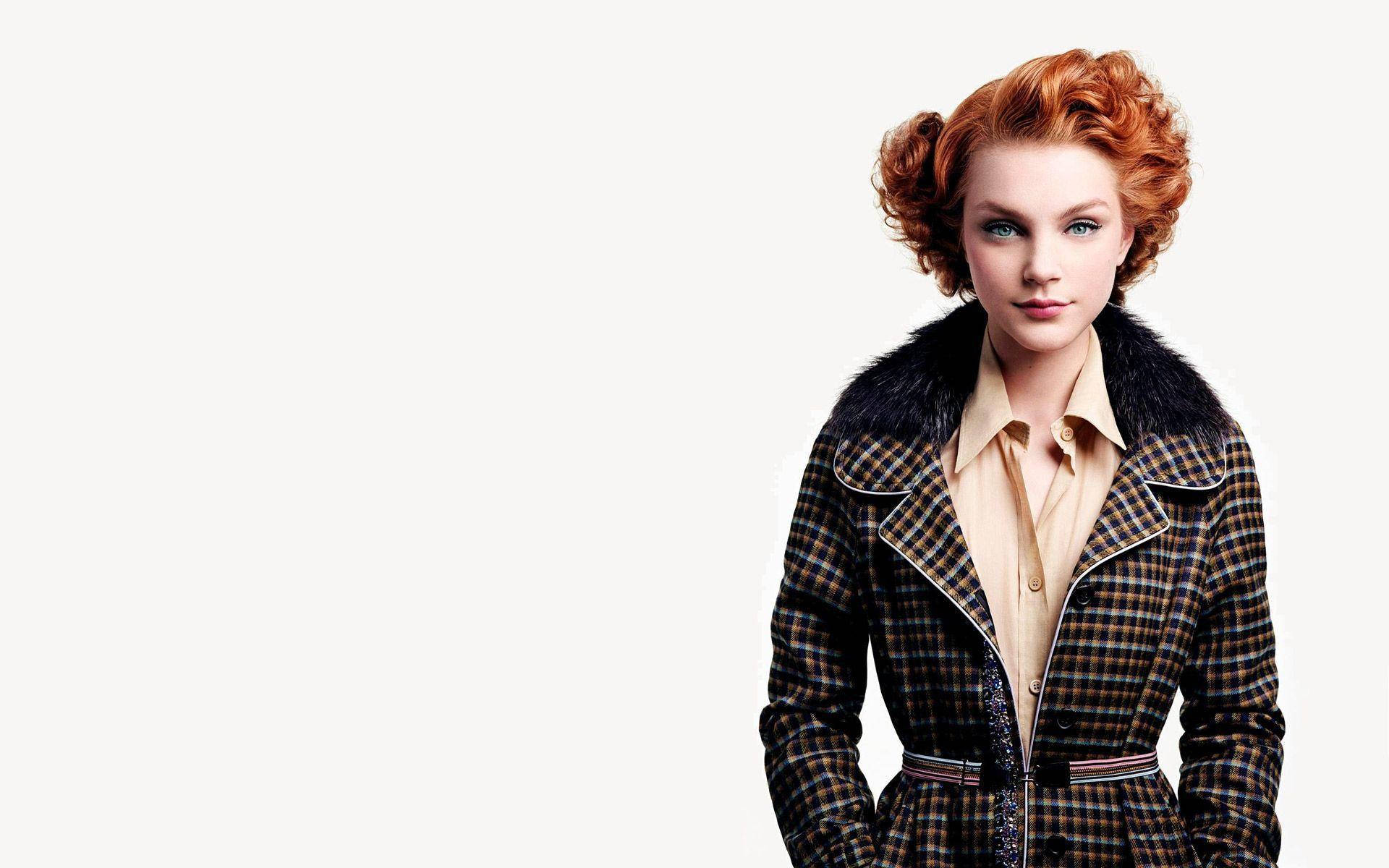 jessica stam 桌布 壁紙 — 一位擁有火紅捲髮和引人注目的藍眼睛的女性，穿著帶有毛領的格子外套，背景為純白色。