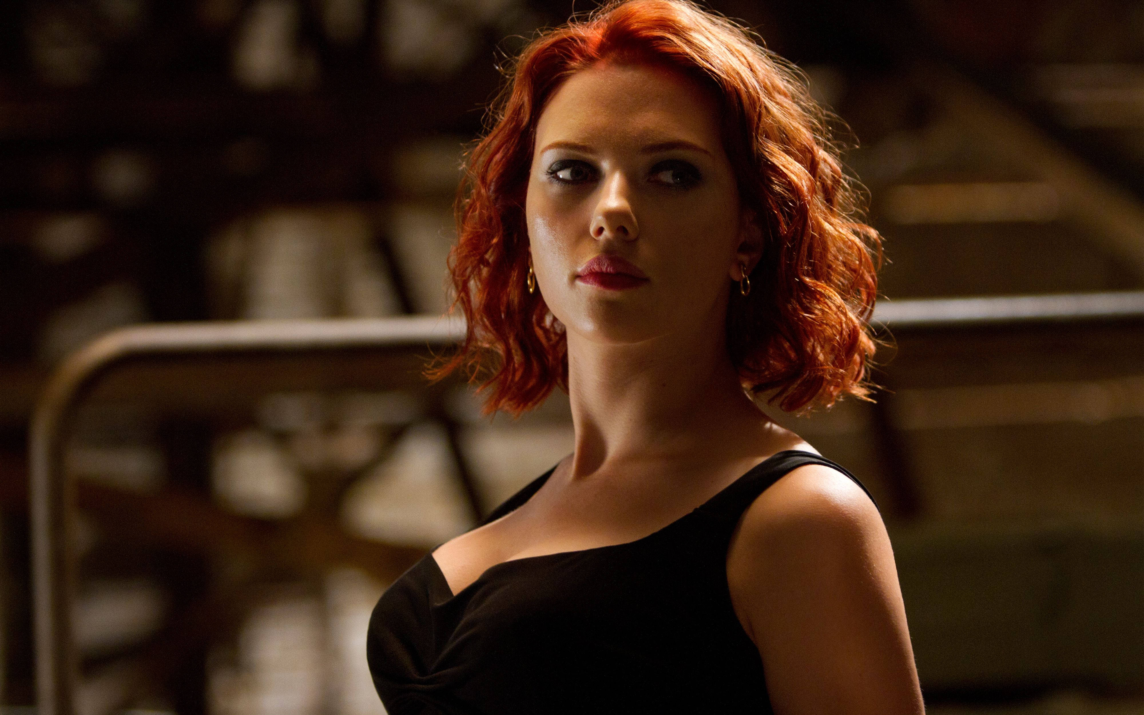 Scarlett Johansson Black Widow 桌布 壁紙 — 一位擁有火紅頭髮和強烈眼神的女性，在昏暗的工業環境中穿著黑色連衣裙。