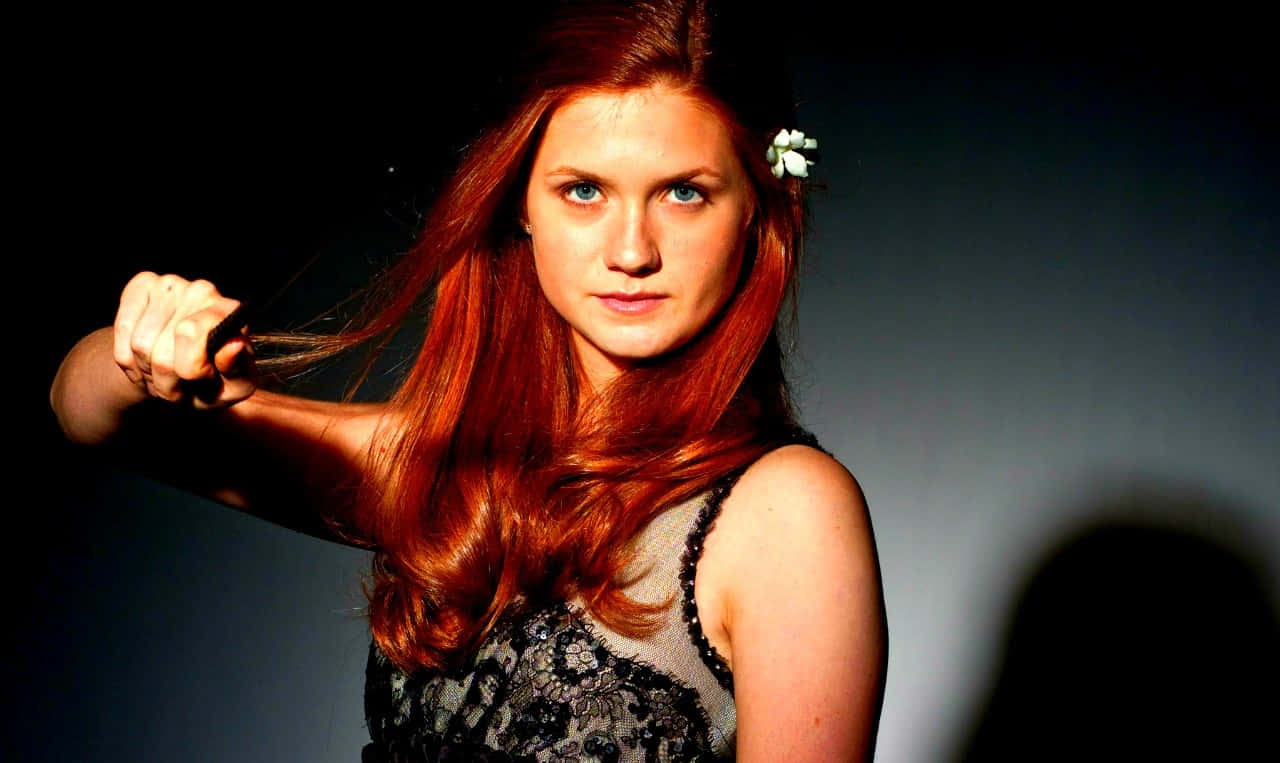 Ginny Weasley 桌布 壁紙 — 一位擁有火紅頭髮和白色花朵在頭髮中的女性，在深色漸變背景前拉緊一條繩子。