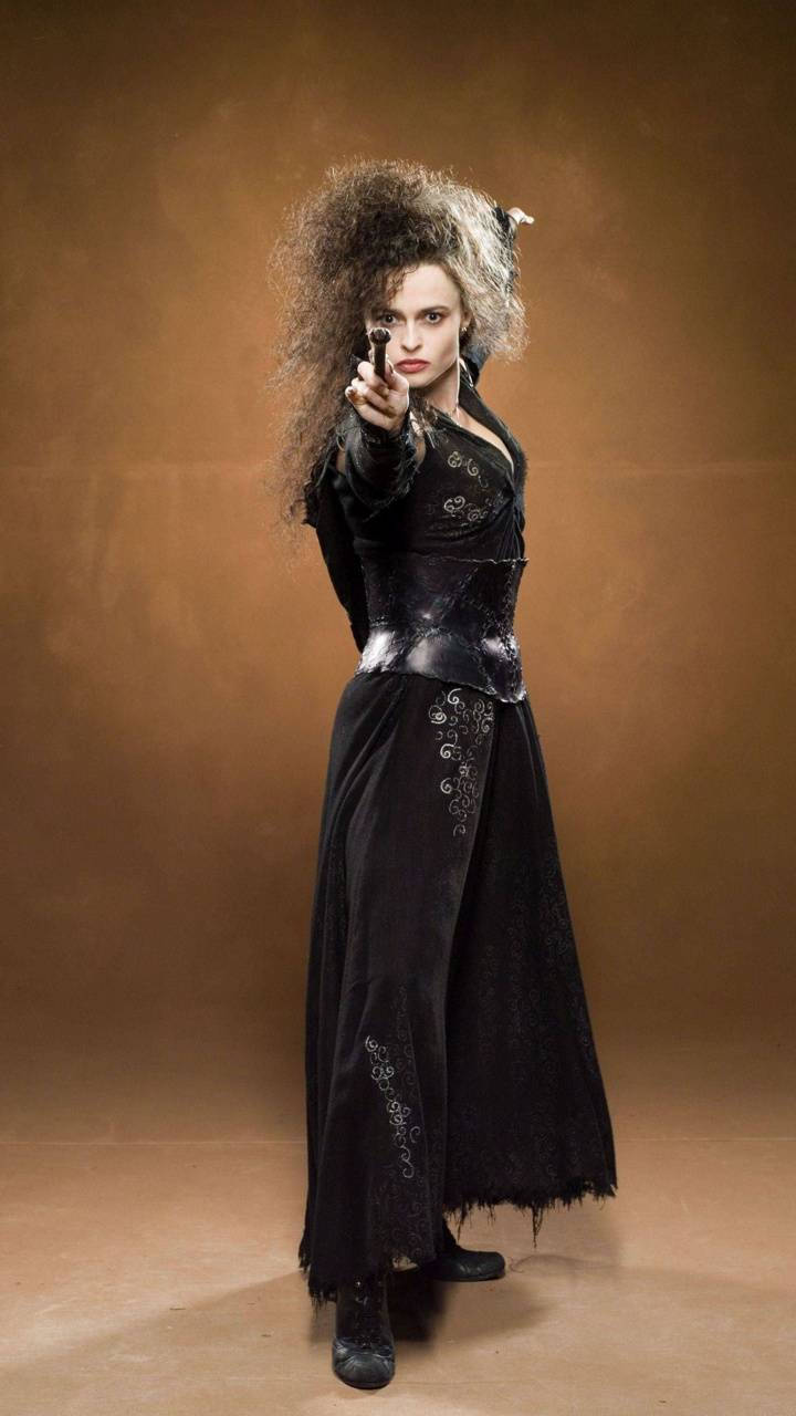 Bellatrix 桌布 壁紙 — 一位擁有狂野捲髮、身穿黑色哥德式長袍的女性，在溫暖的棕色背景下，直接將槍指向觀眾。