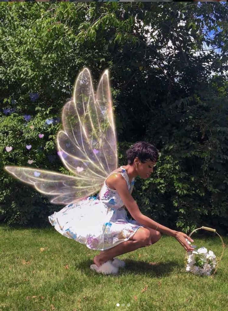 仙女美學 桌布 壁紙 — 一位擁有發光半透明仙女翅膀的女性蹲在陽光明媚的花園中，將白色花朵收集到籃子裡。