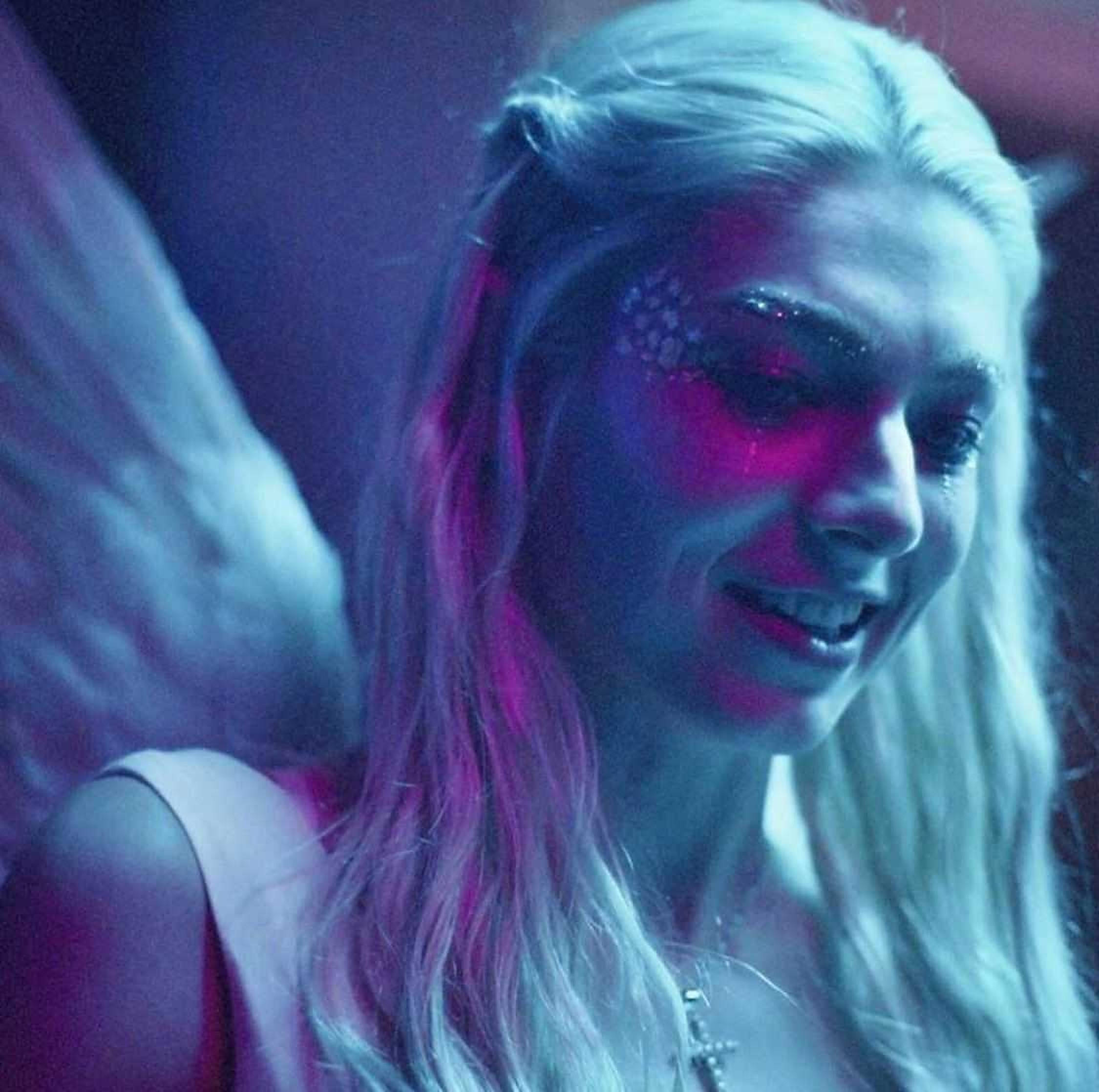 Hunter Schafer 桌布 壁紙 — 一位擁有發光翅膀和閃亮臉部彩繪的女性在霓虹紫和藍色燈光下微笑。