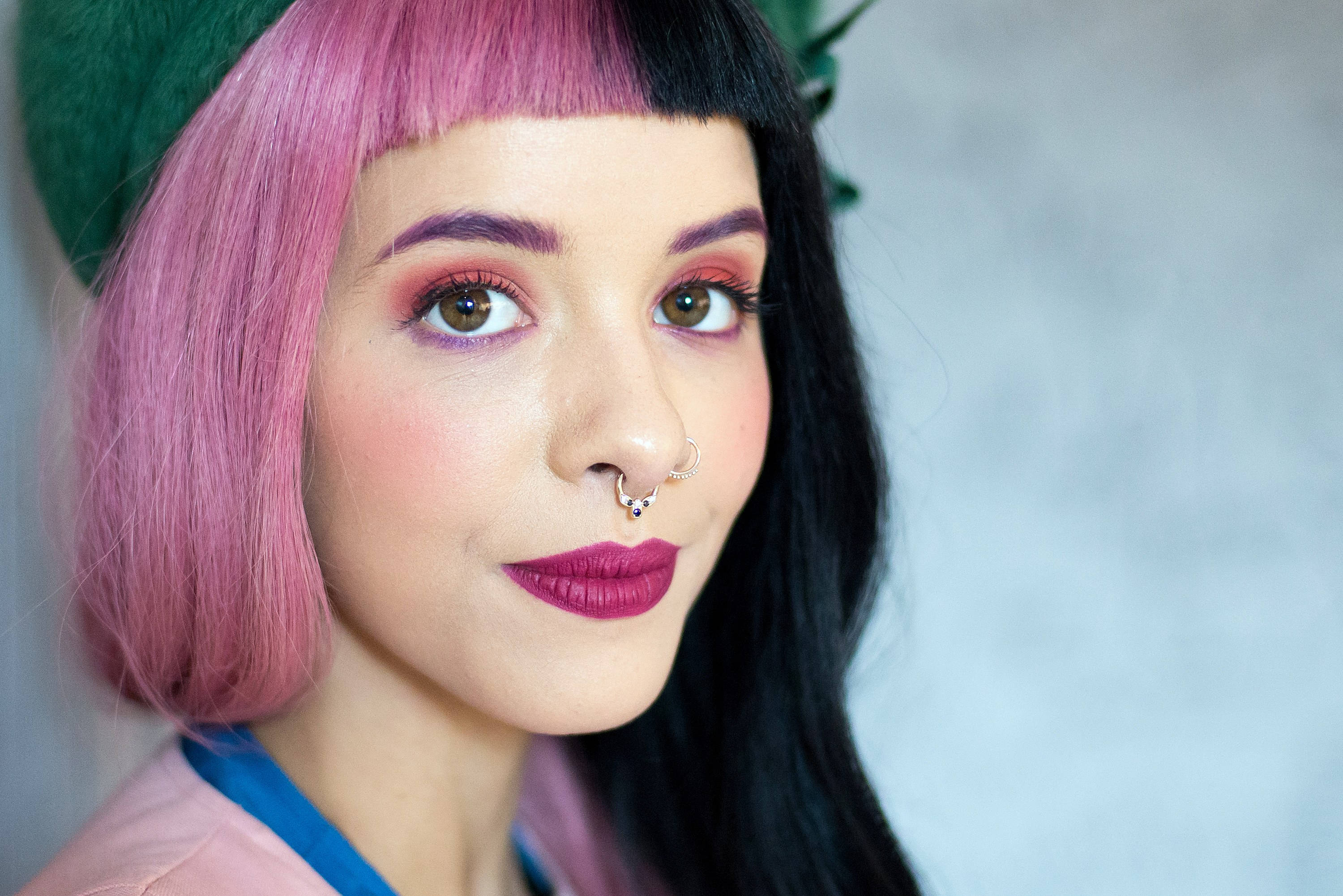 Melanie 桌布 壁紙 — 一位擁有粉紅和黑色頭髮、大膽妝容和鼻環的女性直視鏡頭。