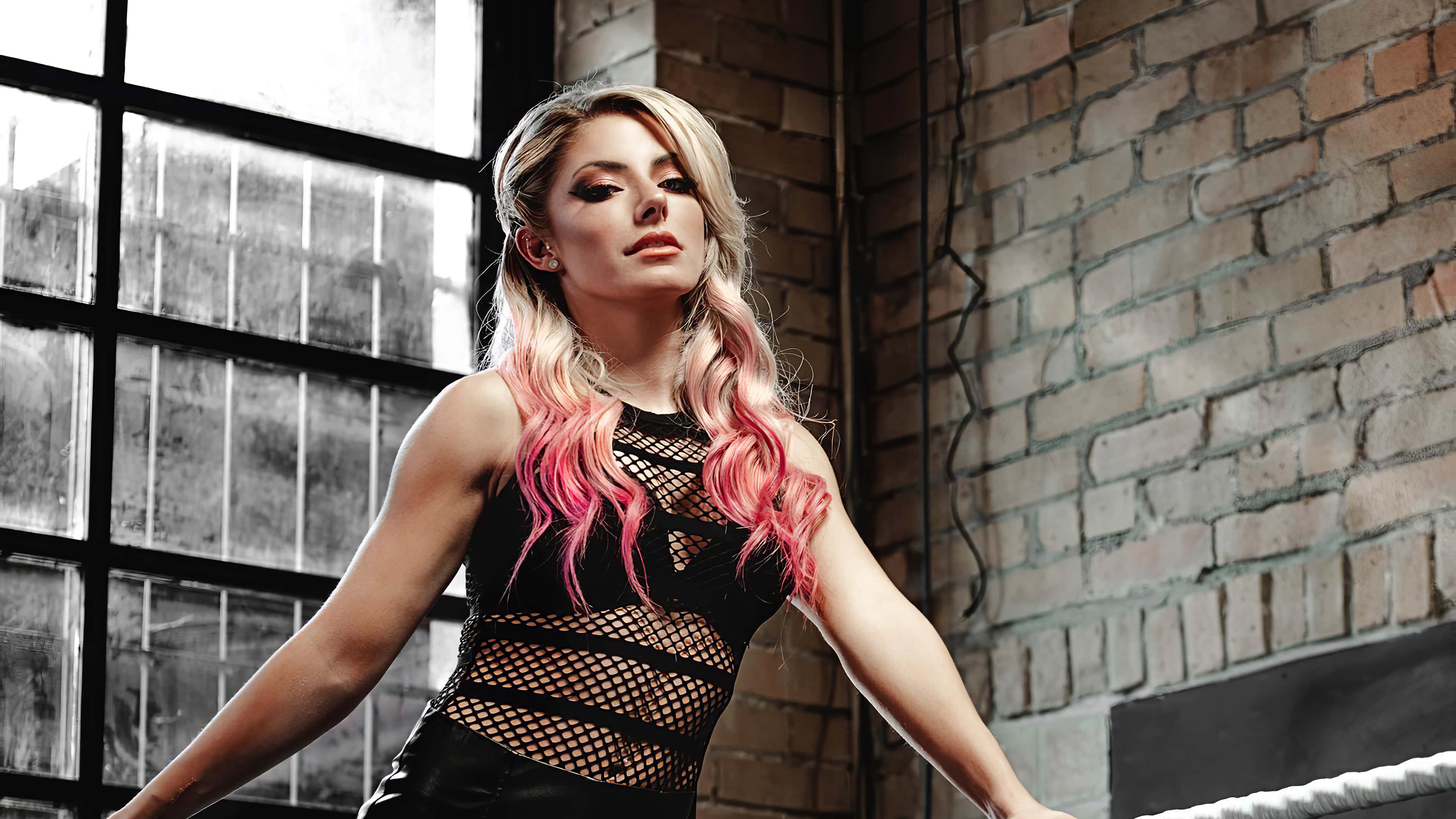 Alexa Bliss 桌布 壁紙 — 一位擁有粉紅挑染金髮、身穿黑色網狀上衣的女性，自信地站在一個有磚牆和大窗戶的房間裡。