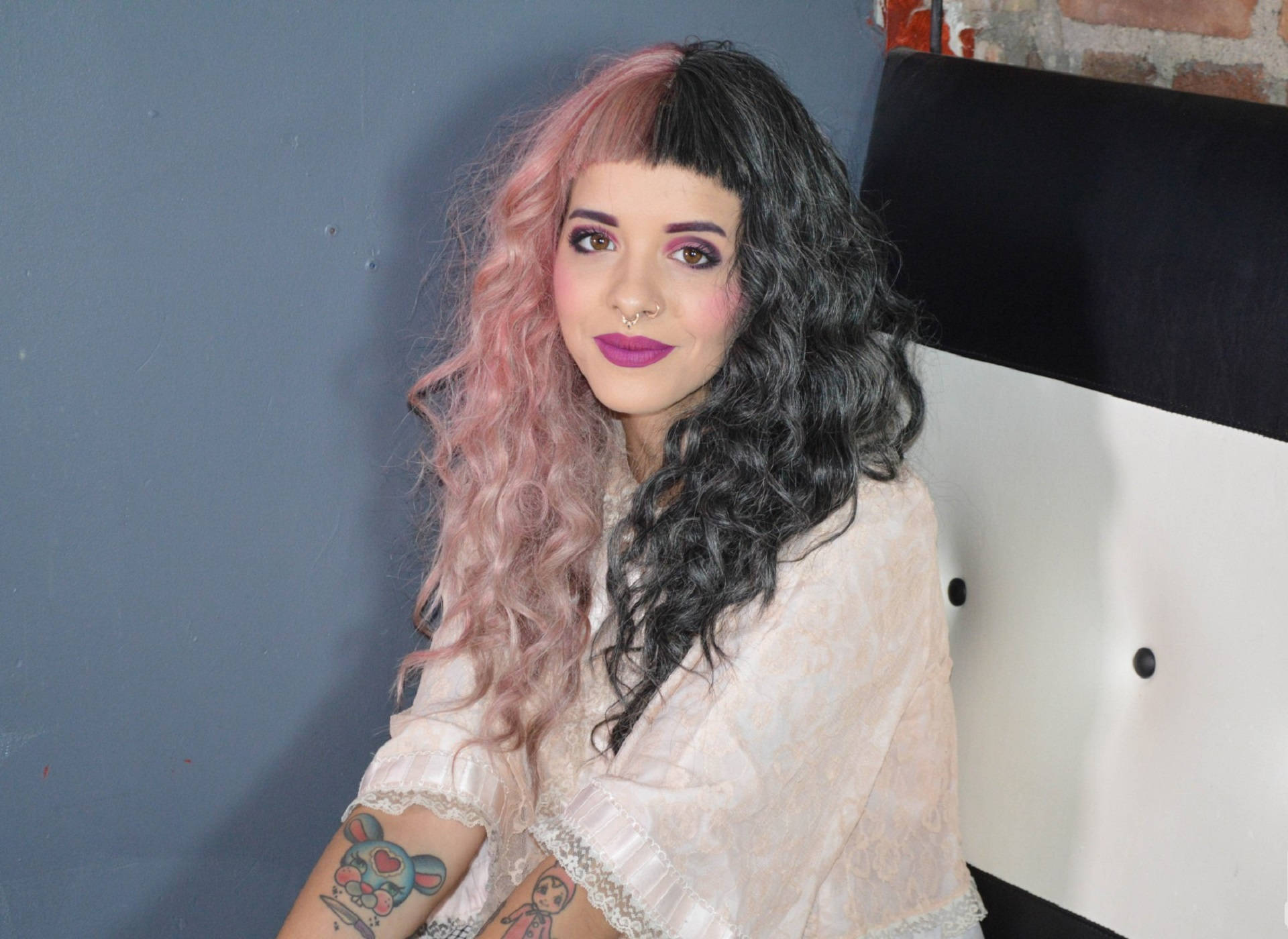 Melanie 桌布 壁紙 — 一位擁有粉紅色和黑色頭髮及紫色唇膏的女性，靠著藍色牆壁和白色椅子坐著。