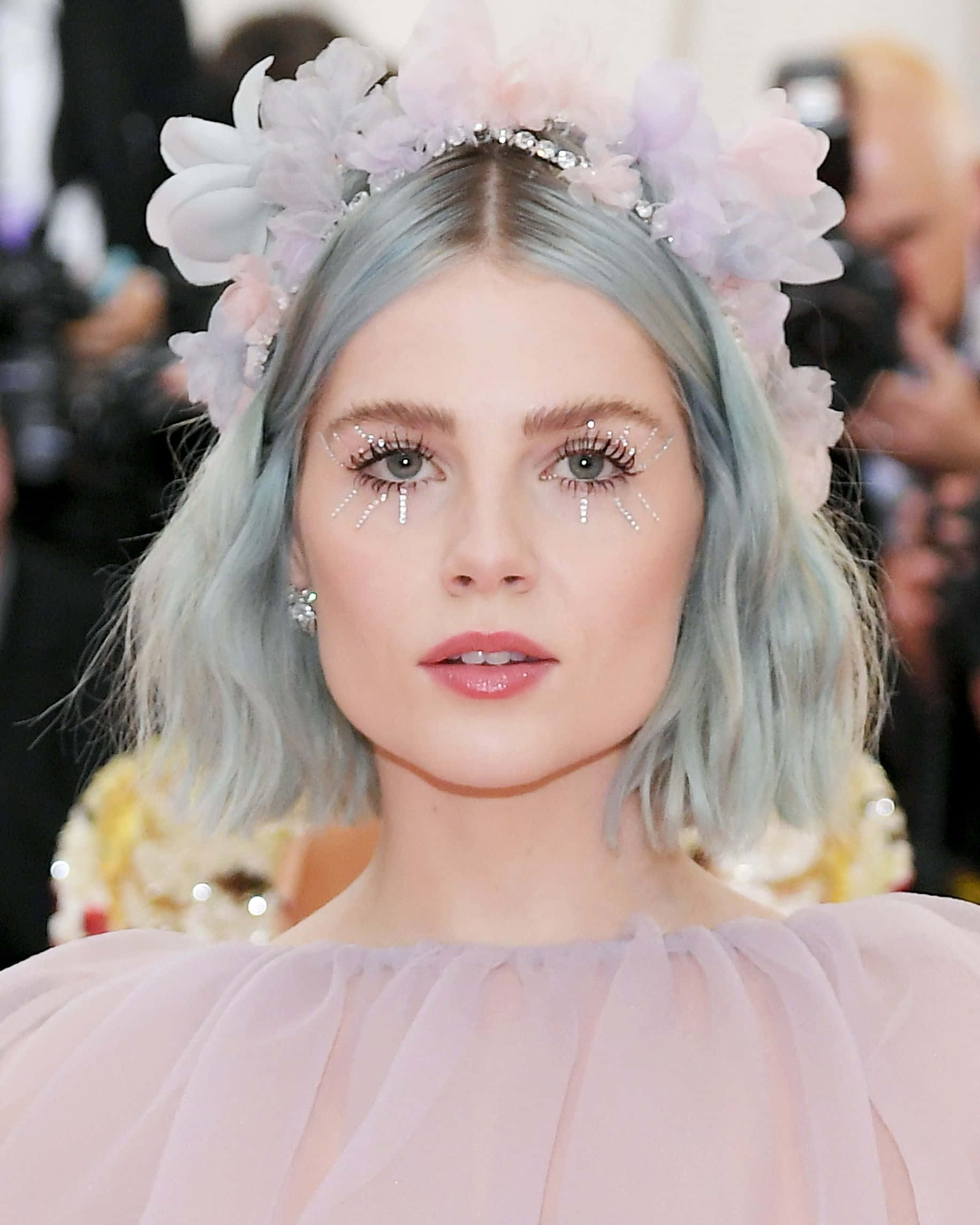Met Gala 桌布 壁紙 — 一位擁有粉藍色頭髮和花冠的女性，帶著閃爍的眼妝和柔軟的粉紅色長袍向前凝視。