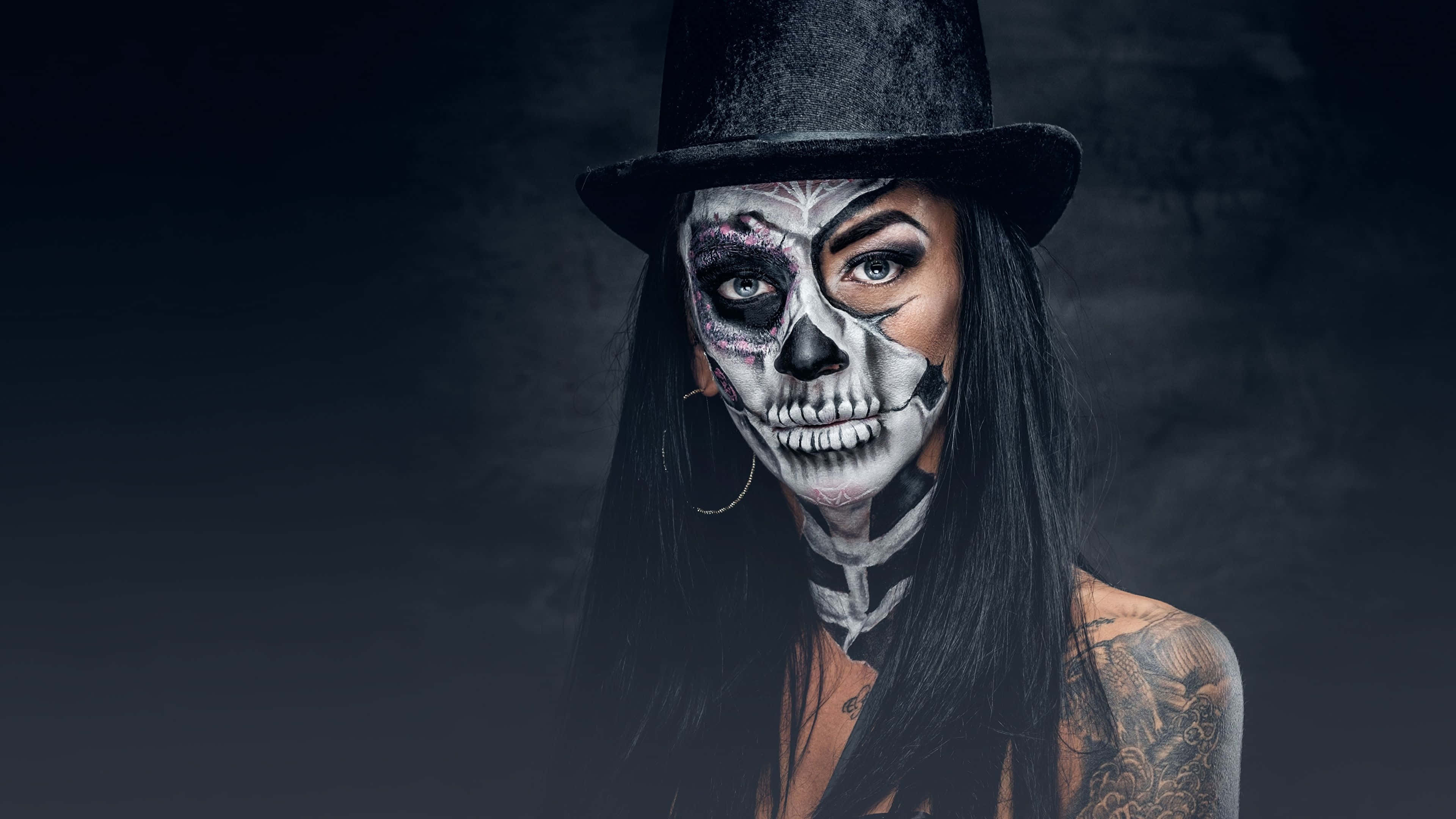 Day Of The Dead 桌布 壁紙 — 一位擁有精緻骷髏妝容和紋身的女性，戴著黑色高頂帽，在深色紋理背景前凝視著。