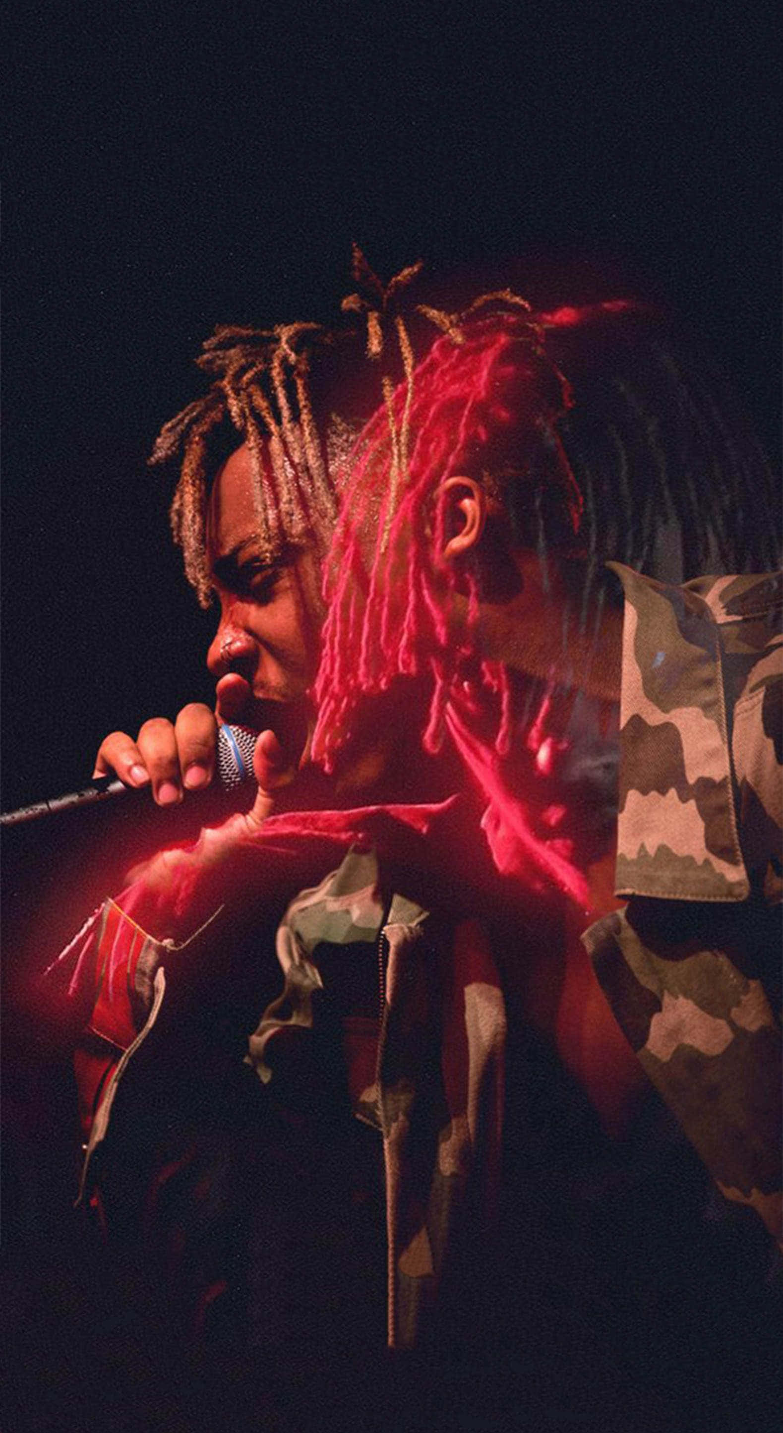 Rappers 桌布 壁紙 — 一位擁有紅色發光辮子的說唱歌手在黑暗的舞台燈光下，穿著迷彩外套對著麥克風唱歌。