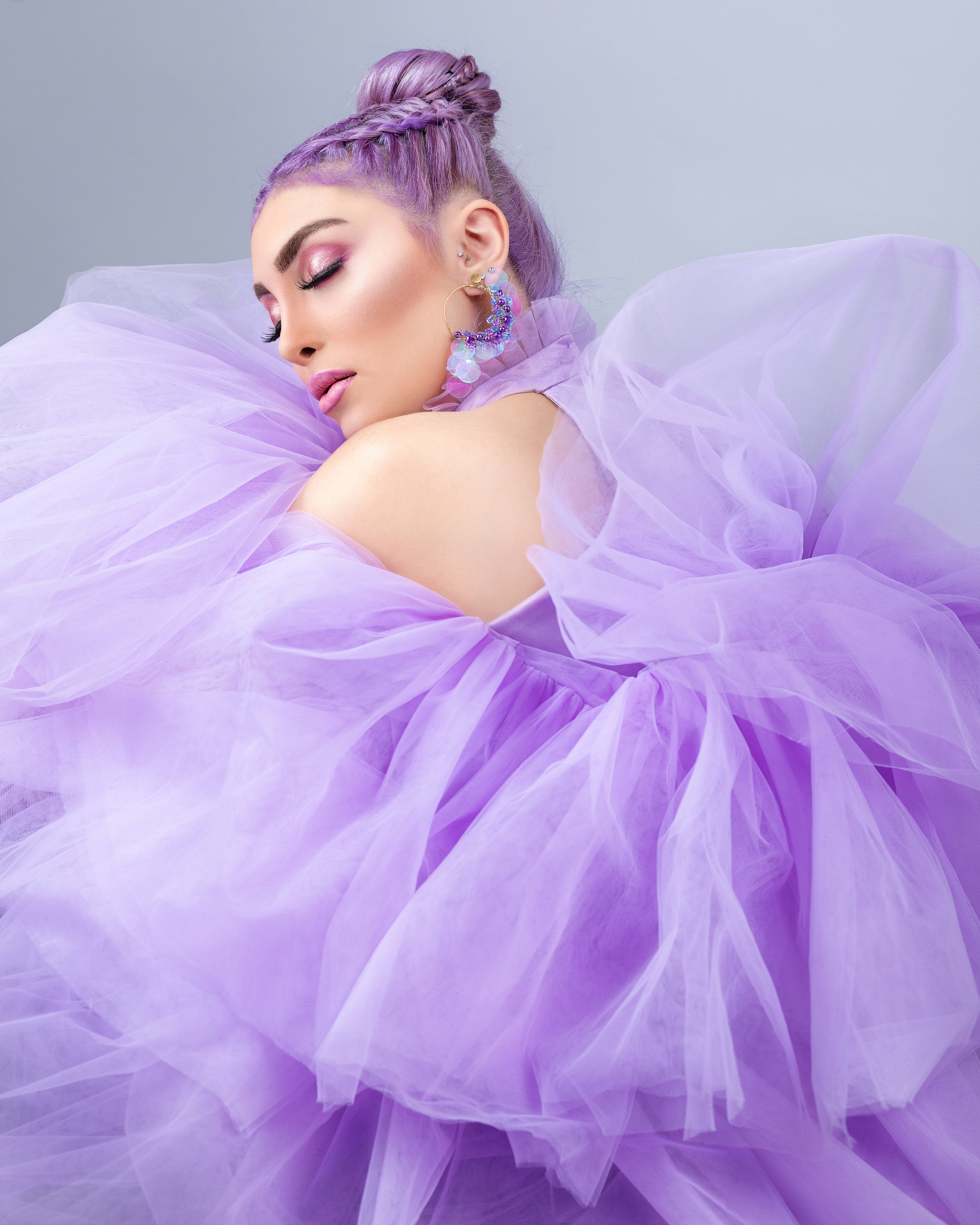 時尚 桌布 壁紙 — 一位擁有紫色辮子頭髮和相配薄紗長裙的女性，在柔和的灰色背景前優雅地擺姿勢。