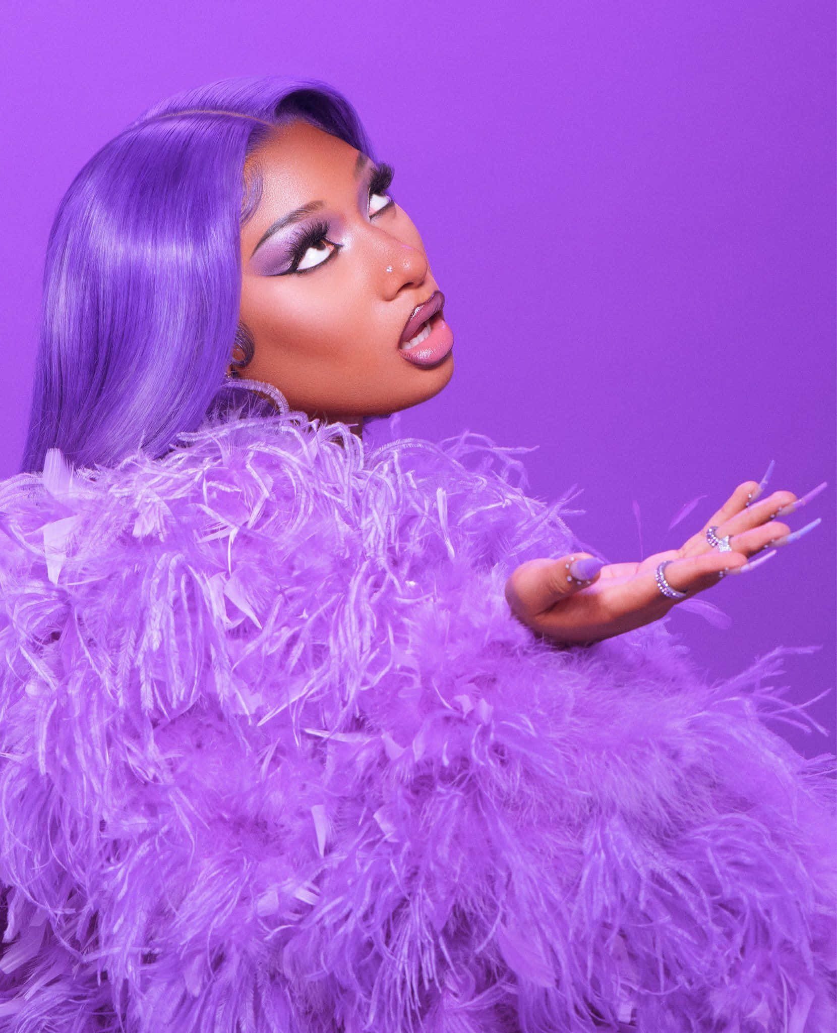 Megan Thee Stallion 桌布 壁紙 — 一位擁有紫色頭髮、穿著紫色羽毛服裝的女性，在純紫色背景前擺姿勢。