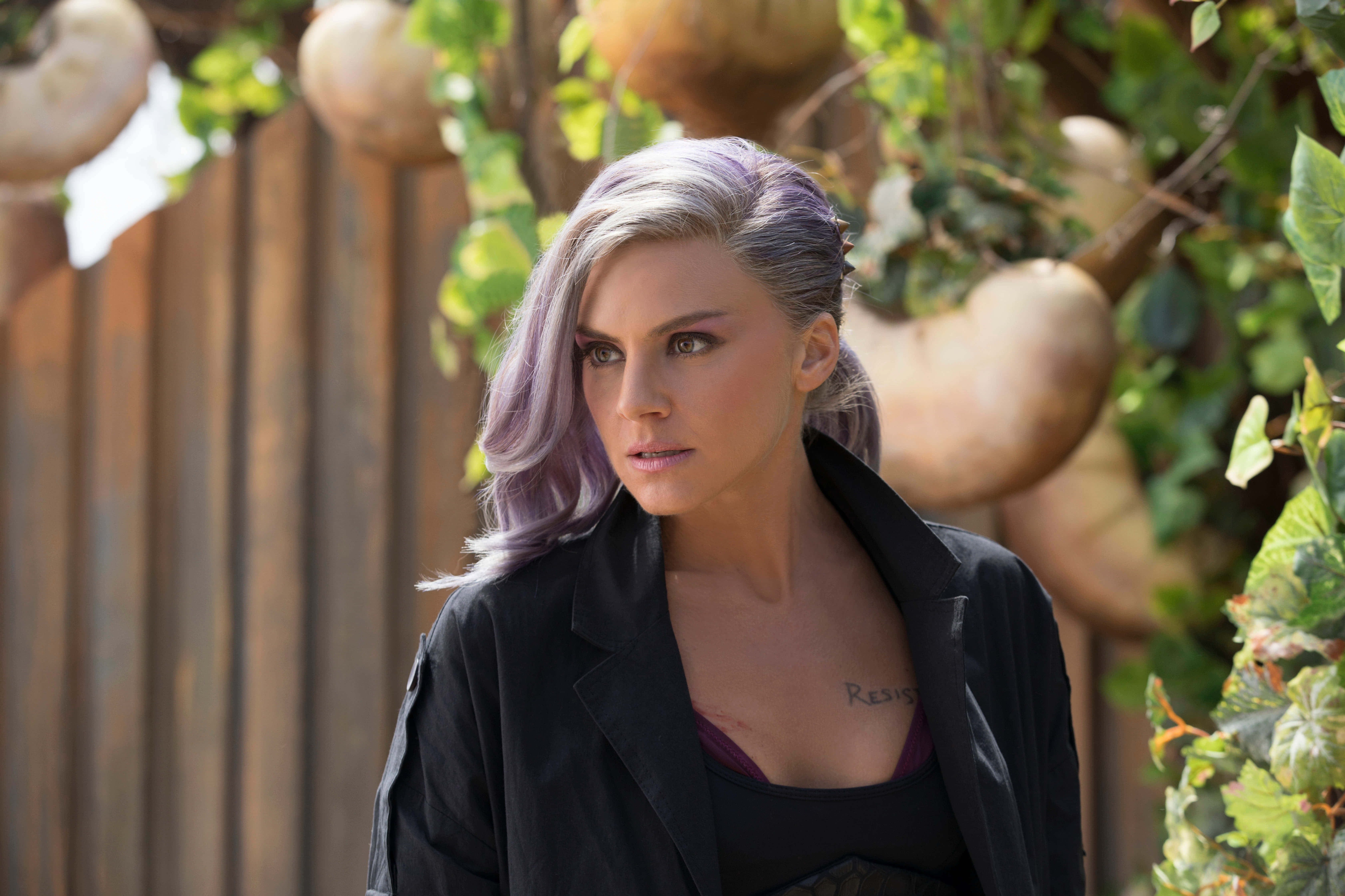 eliza coupe 桌布 壁紙 — 一位擁有紫色頭髮和「Resist」刺青的女性，對著一個裝飾著懸掛葫蘆和綠色藤蔓的木柵欄凝視。