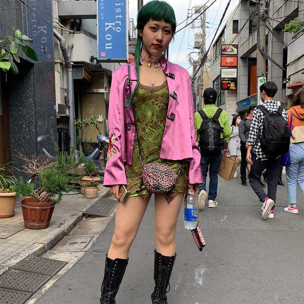 Harajuku Fashion 桌布 壁紙 — 一位擁有綠色頭髮和鮮豔粉紅色外套的年輕女性自信地站在繁忙的東京街道上，周圍是行人和城市標誌。