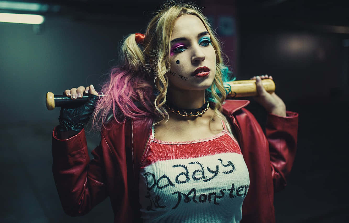 Harley Quinn Cosplay 桌布 壁紙 — 一位擁有色彩繽紛頭髮和化妝的女性，在昏暗的城市環境中將棒球棍扛在肩上。