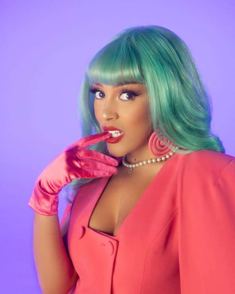 Doja Cat 桌布 壁紙 — 一位擁有藍綠色頭髮和粉紅色手套的女性，在紫色背景前穿著大膽的粉紅色服裝，俏皮地擺姿勢。