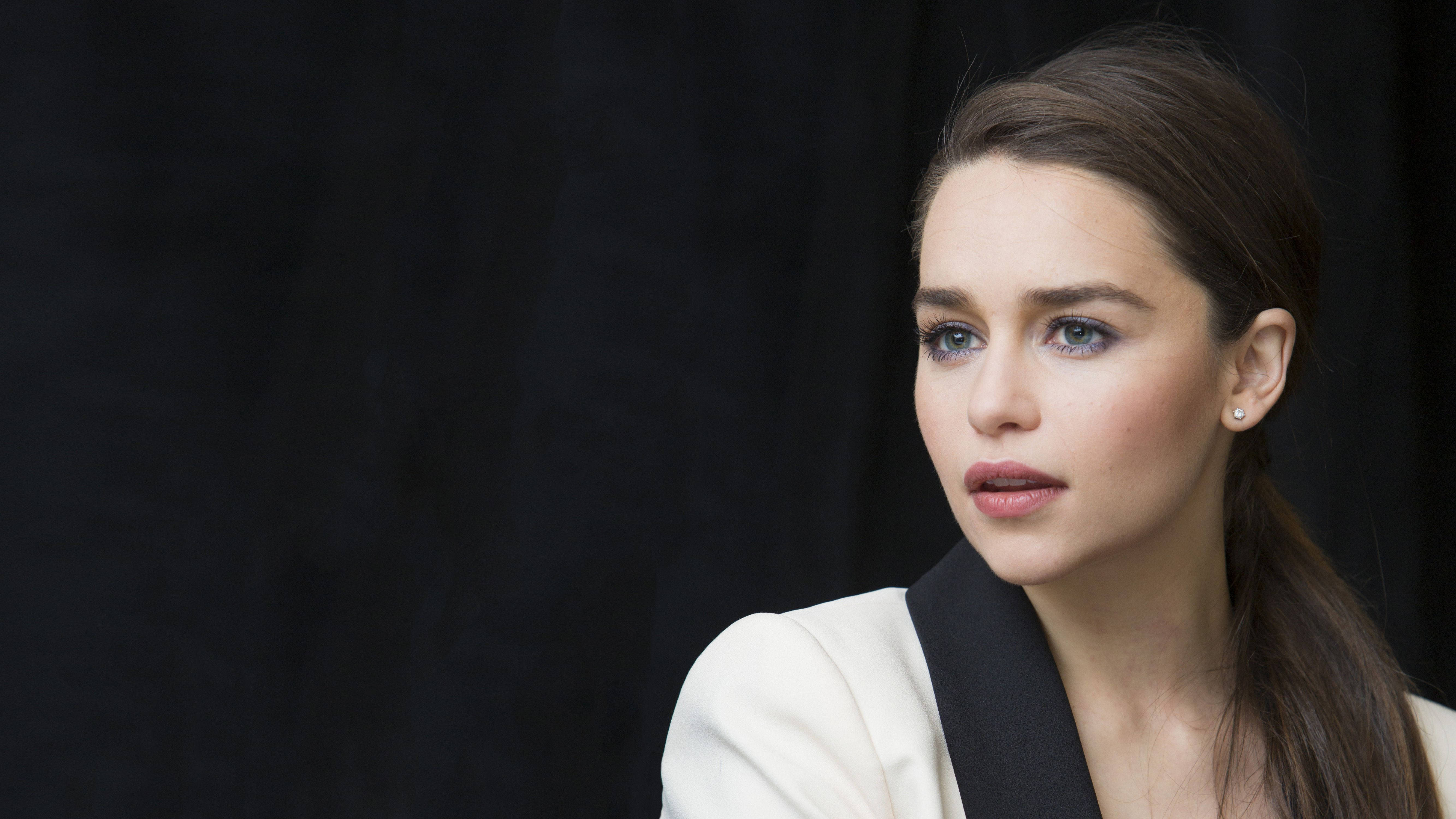 Emilia 桌布 壁紙 — 一位擁有藍色眼睛和棕色馬尾辮的女性，在黑暗背景下穿著白色和黑色的服裝，若有所思地凝視著。