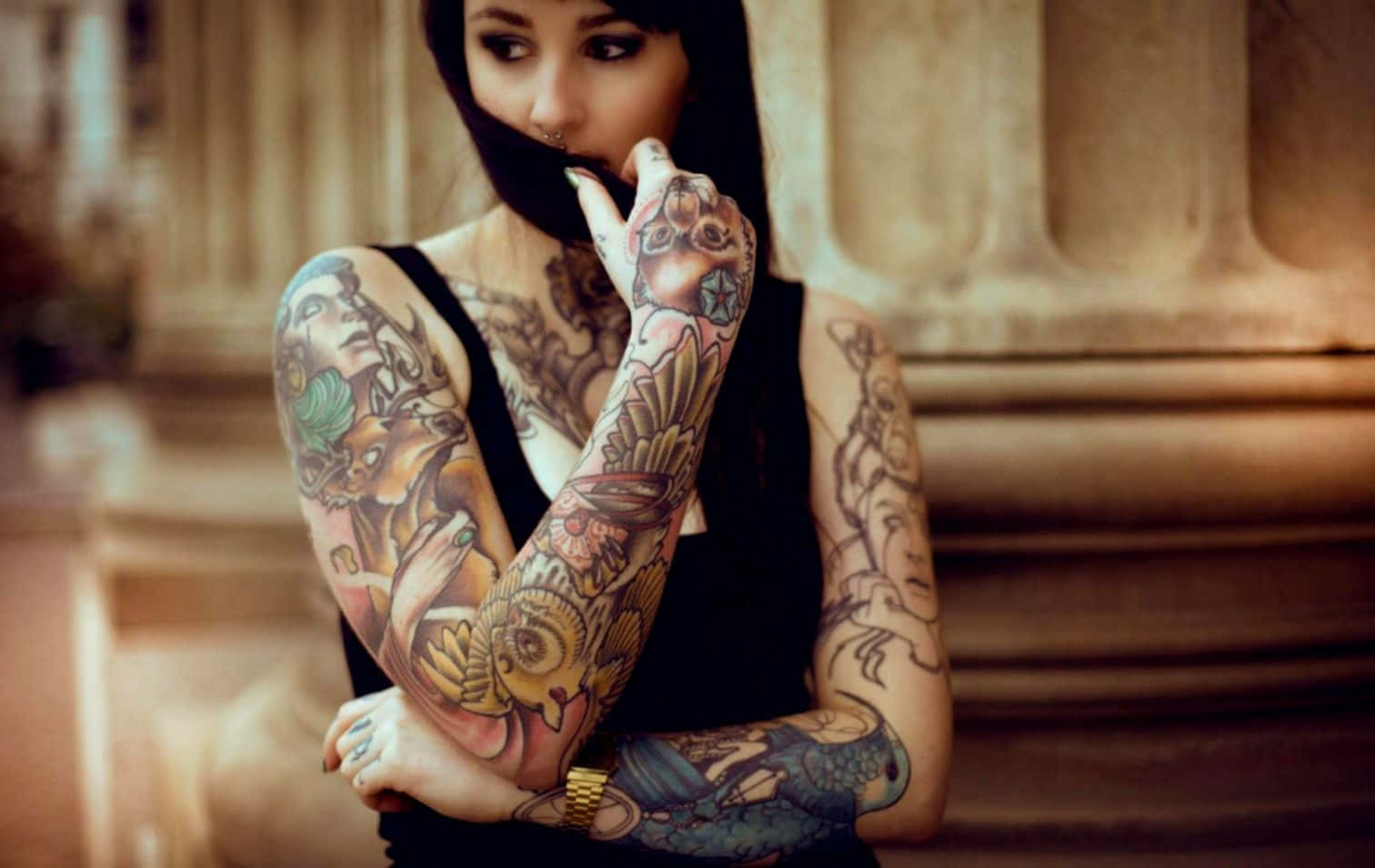 Tattoo Girl 桌布 壁紙 — 一位擁有複雜彩色刺青的女性，在經典石柱背景下遮住嘴巴。