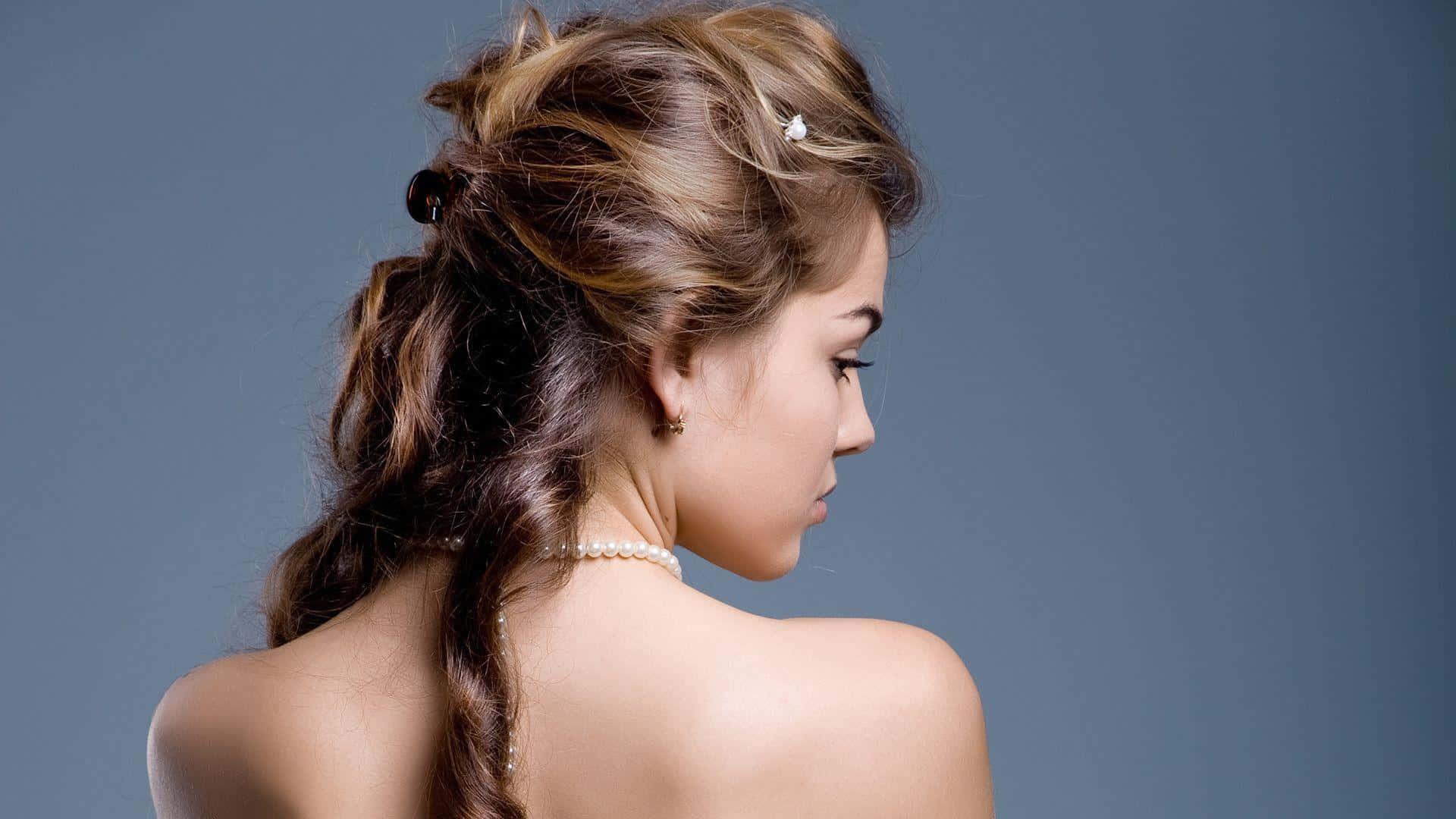 Hairstyle 桌布 壁紙 — 一位擁有複雜辮子頭髮和珍珠項鍊的女性，在柔和的藍色工作室背景下向下凝視。