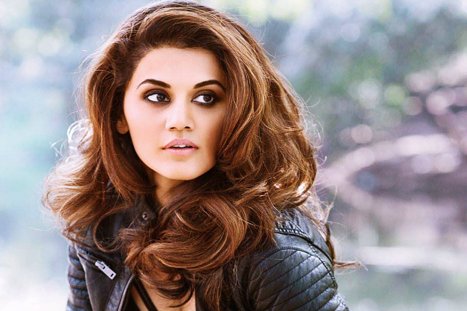 Taapsee Pannu 桌布 壁紙 — 一位擁有豐盈棕色頭髮和濃妝豔抹的女性，穿著黑色絎縫皮夾克，專注地凝視著。