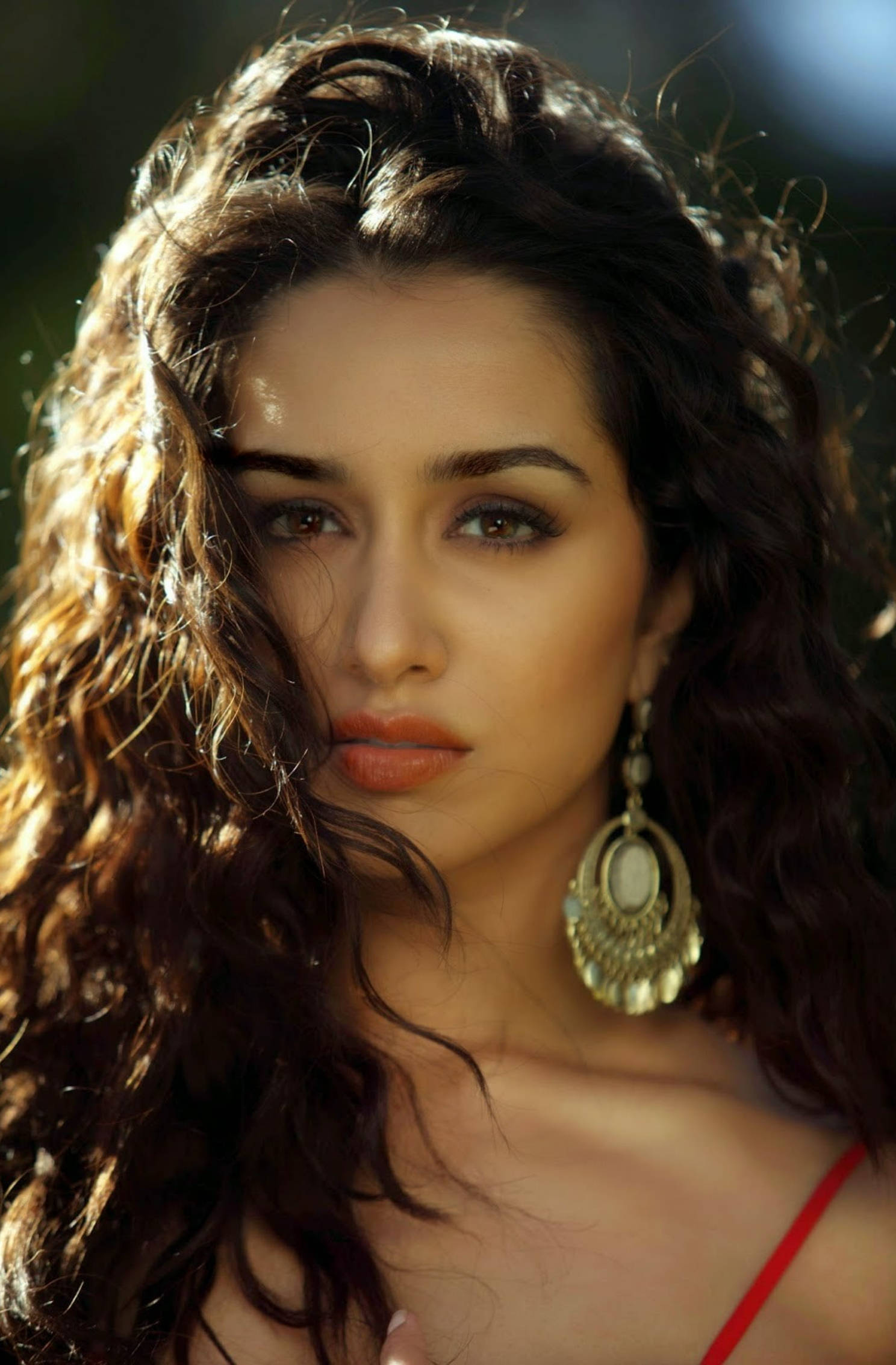 Shraddha Kapoor 桌布 壁紙 — 一位擁有豐盈深色捲髮和金色耳環的女性，在溫暖陽光穿過樹葉灑落時溫柔地凝視。