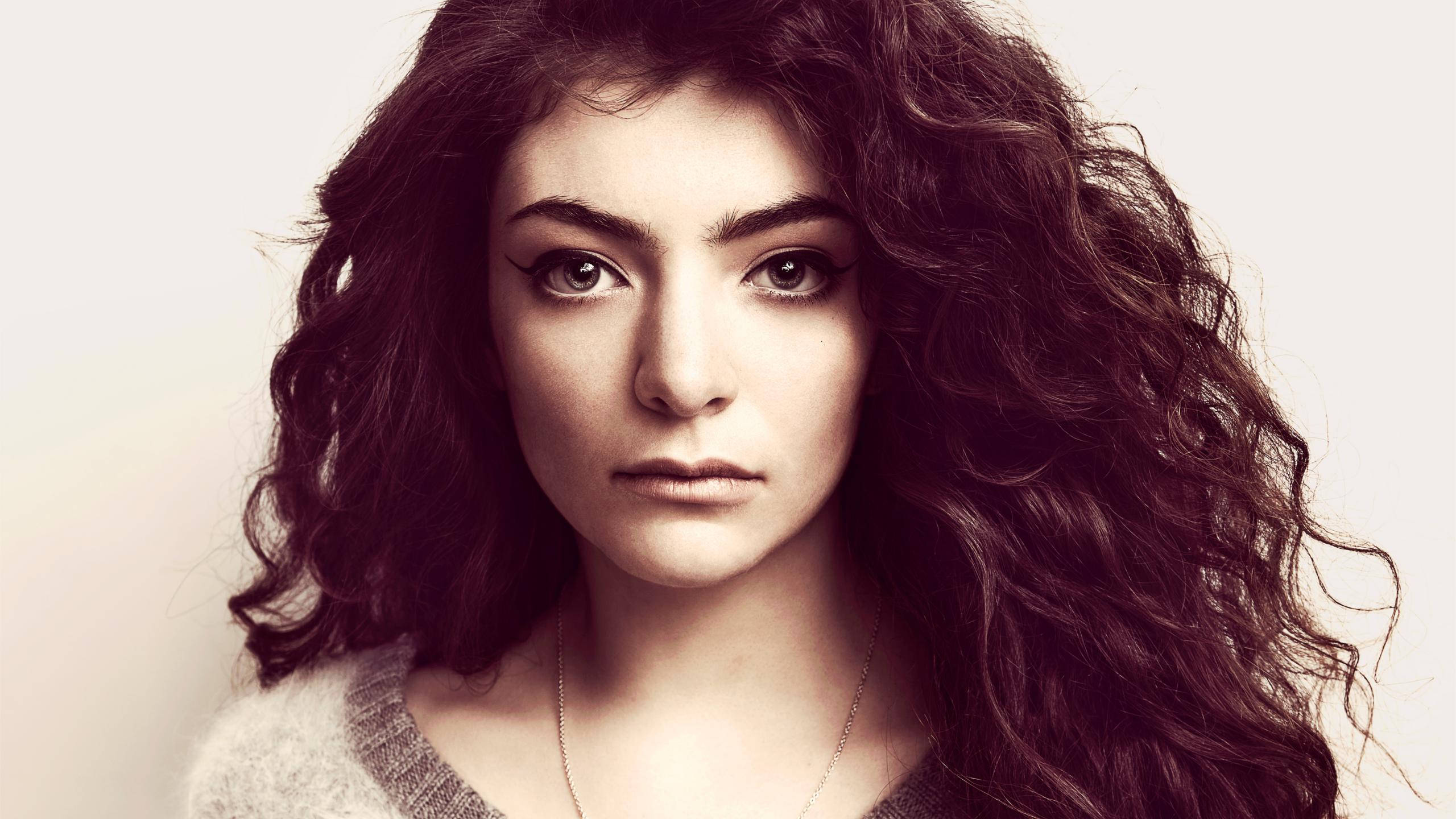 Lorde 桌布 壁紙 — 一位擁有豐盈深色捲髮的女性，在柔和的中性背景前凝視著。