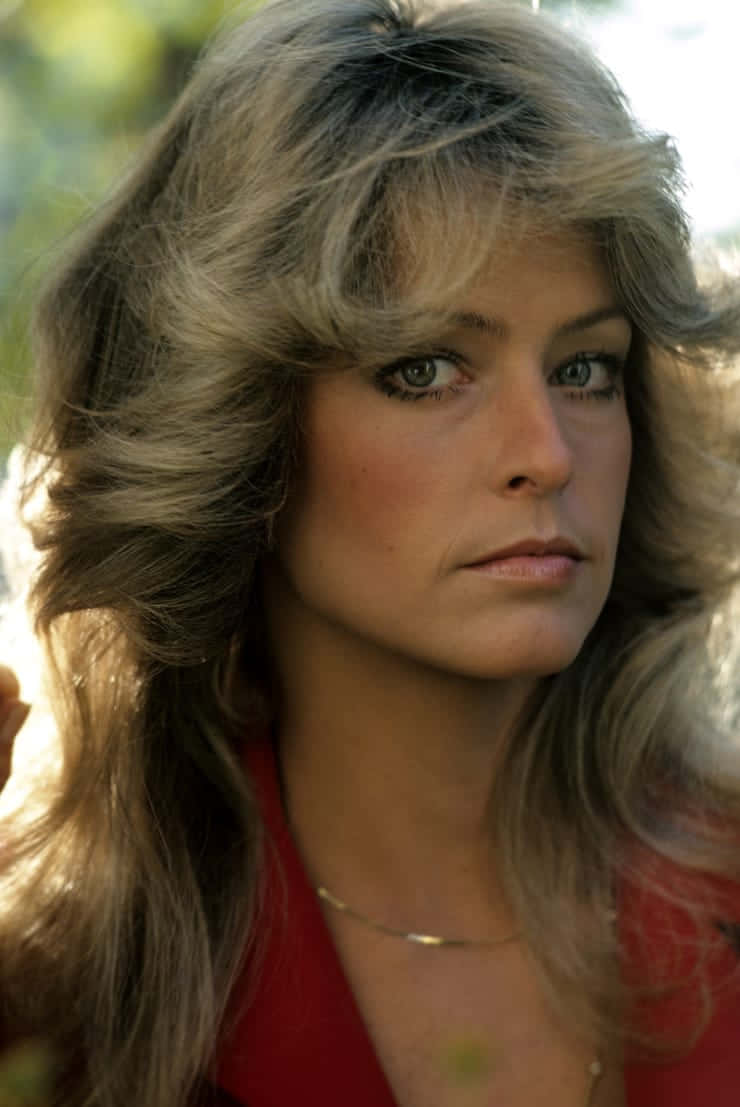 Farrah Fawcett 桌布 壁紙 — 一位擁有豐盈金髮和綠色眼睛的女性在柔和的自然光下戶外沉思地凝視。