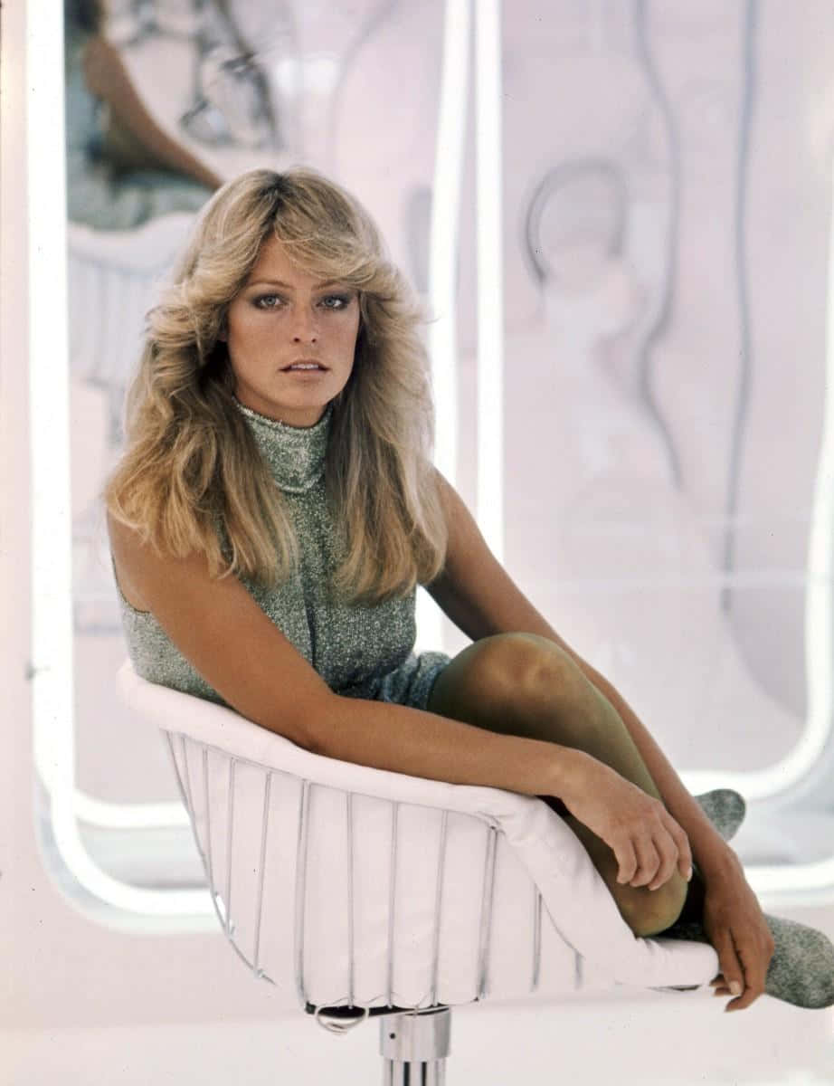 Farrah Fawcett 桌布 壁紙 — 一位擁有豐盈金髮的女性，端坐在白色現代椅子上，背景是柔和照明的抽象風格。