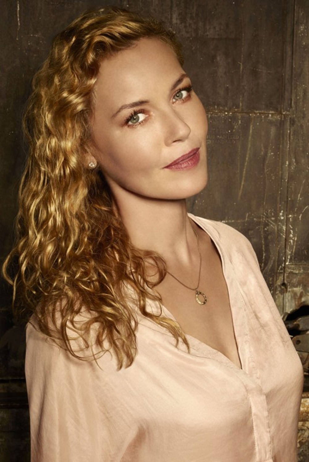 Actress HD 桌布 壁紙 — 一位擁有金色捲髮和柔軟粉紅色襯衫的女性，對著有紋理的深色牆壁若有所思地凝視。