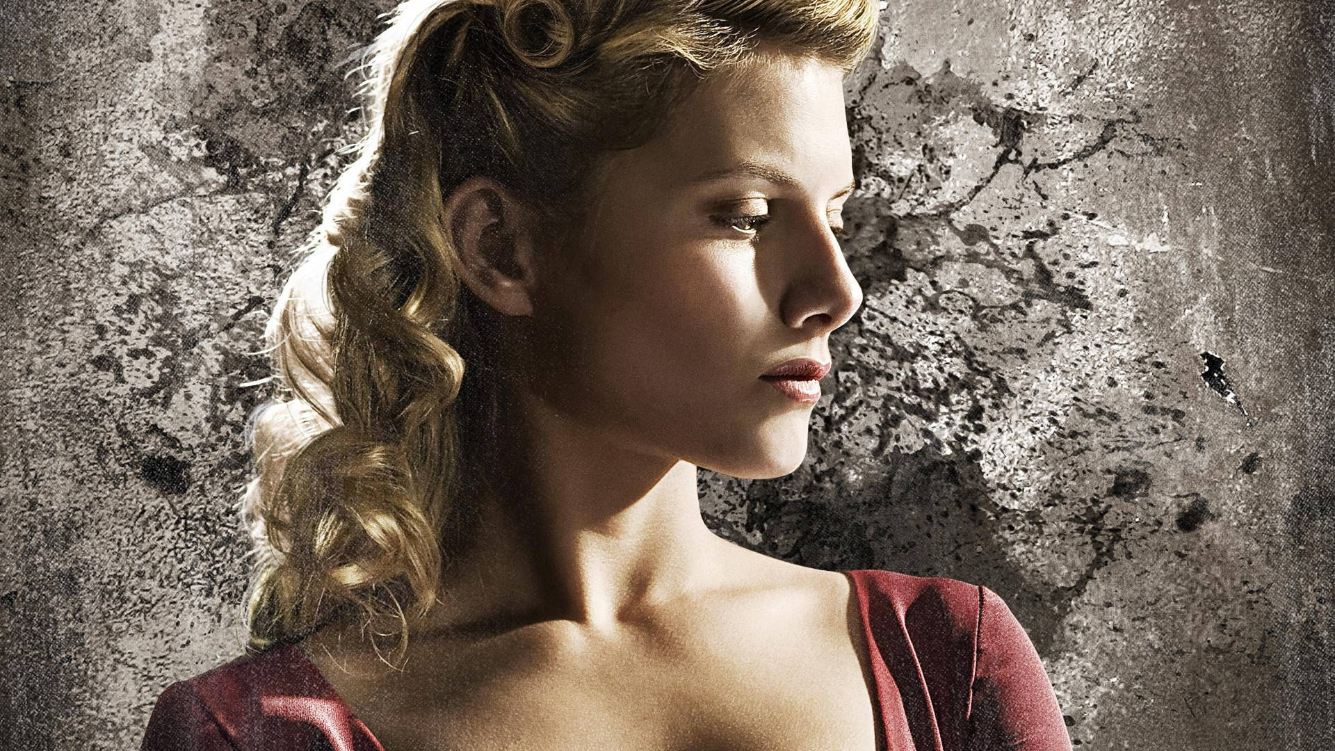 Inglourious Basterds 桌布 壁紙 — 一位擁有金色捲髮和紅色連衣裙的女性，在戲劇性的燈光下，對著風化的灰色牆壁向下凝視。