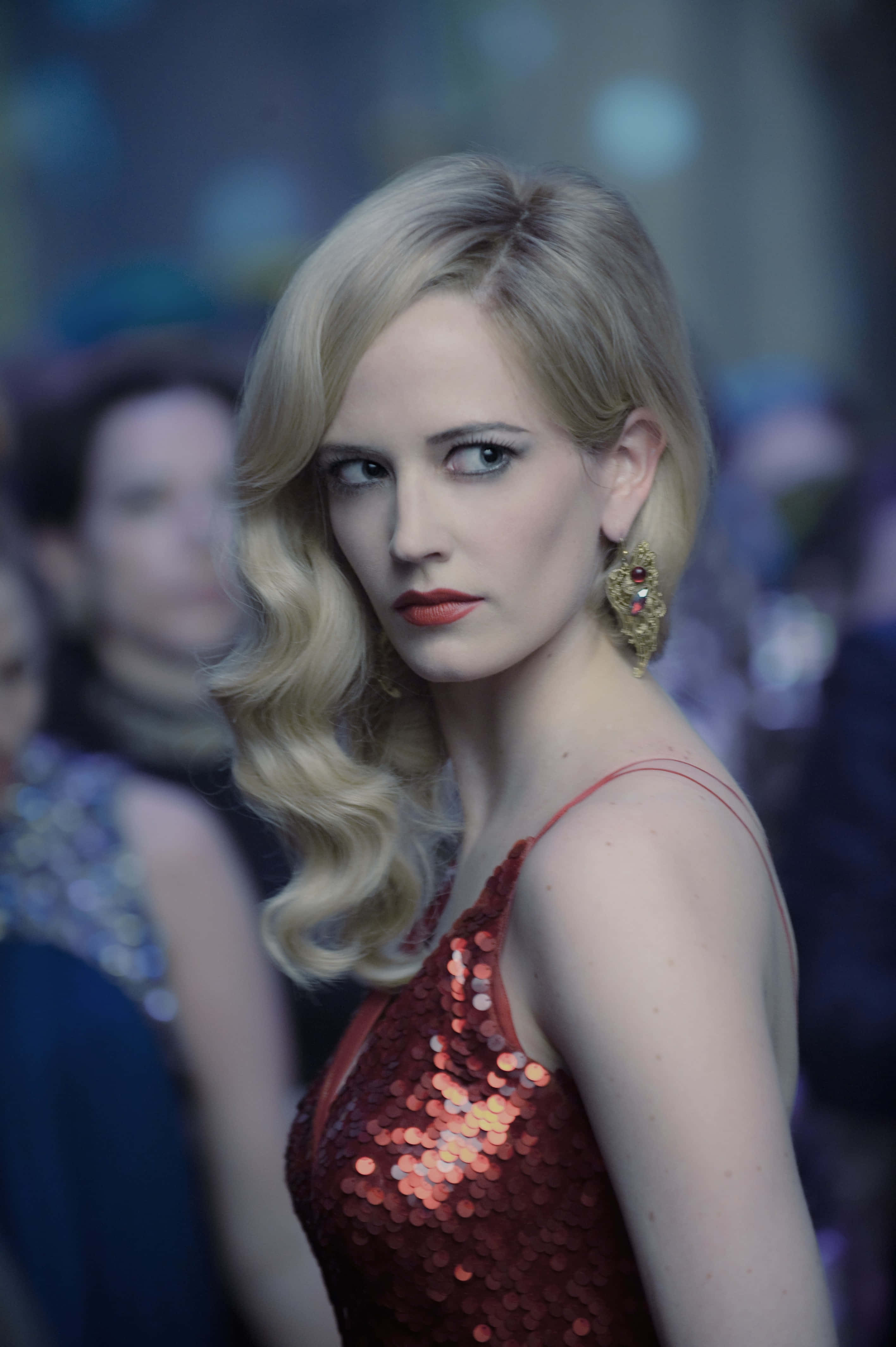 eva green 桌布 壁紙 — 一位擁有金色波浪捲髮、身穿紅色亮片連衣裙的女性，在昏暗的派對場景中越過肩膀怒視。