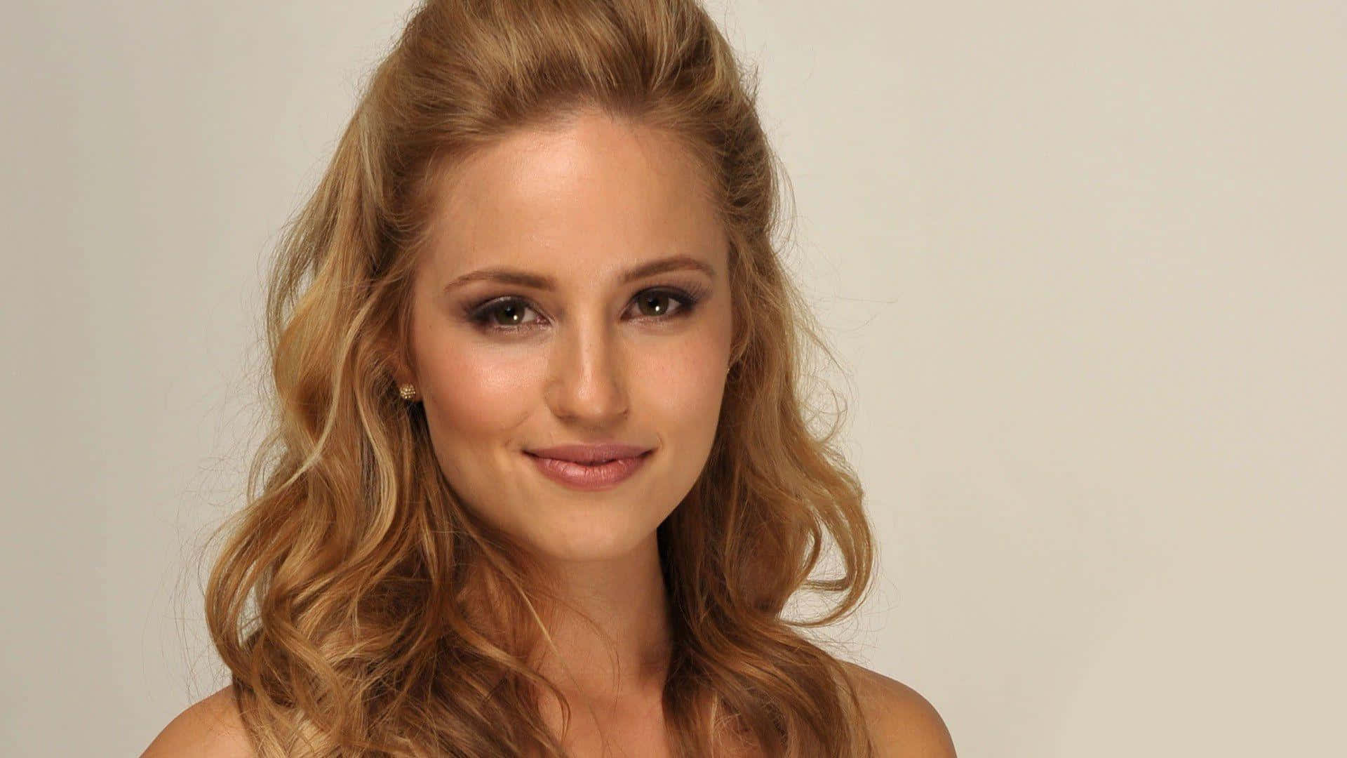 dianna agron 桌布 壁紙 — 一位擁有金色波浪長髮和溫柔微笑的女性，在純色淺色背景前擺姿勢。