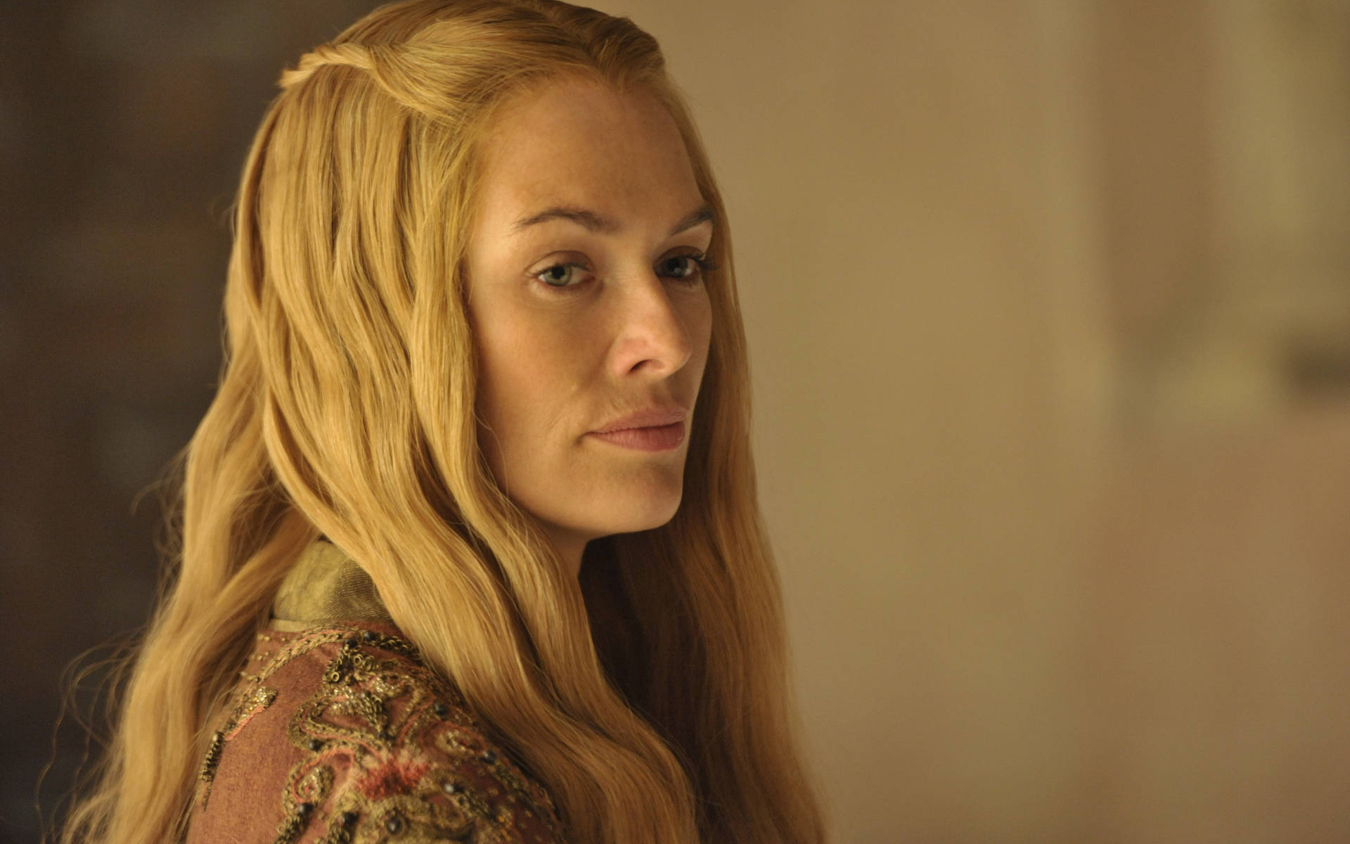 cersei lannister 桌布 壁紙 — 一位擁有金色長髮、表情嚴肅的女性，穿著暖色調的華麗刺繡服裝。