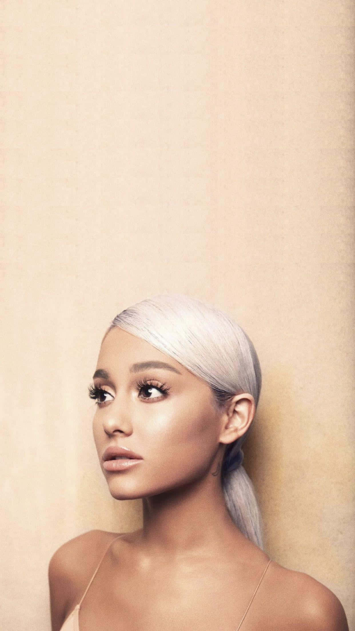 Aesthetic Ariana Grande 桌布 壁紙 — 一位擁有鉑金色頭髮、梳著俐落馬尾的女性，在柔和的米色紋理牆壁前若有所思地凝視。
