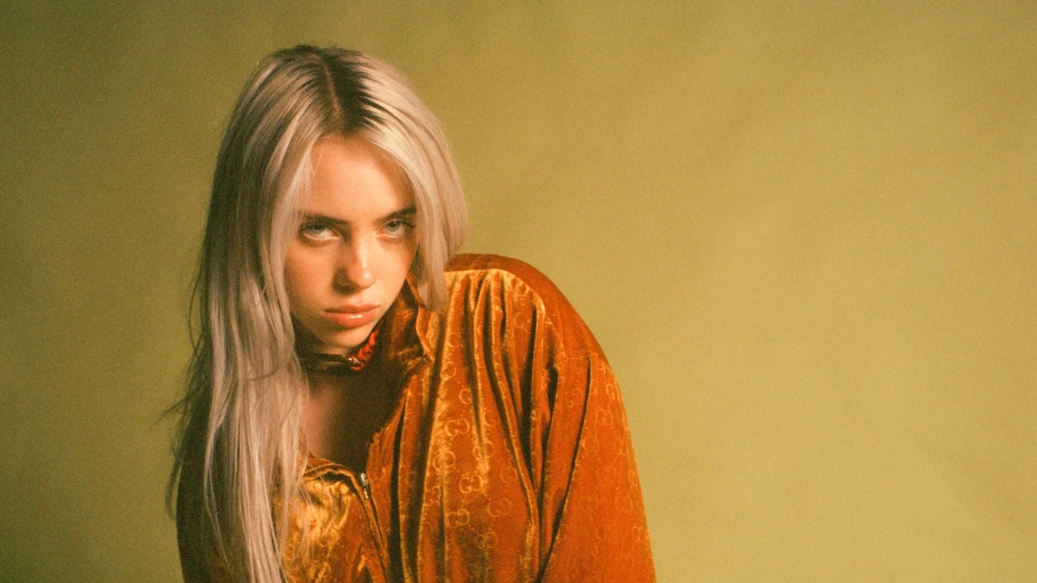 Billie Eilish Laptop 桌布 壁紙 — 一位擁有鉑金色頭髮的女性，在柔和的綠色背景下穿著華麗的橙色天鵝絨服裝。