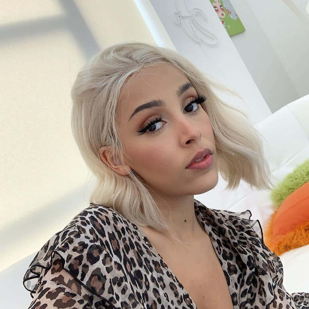 Doja Cat 桌布 壁紙 — 一位擁有鉑金色鮑伯頭和濃密睫毛的女性，在明亮的陽光下室內穿著豹紋襯衫。