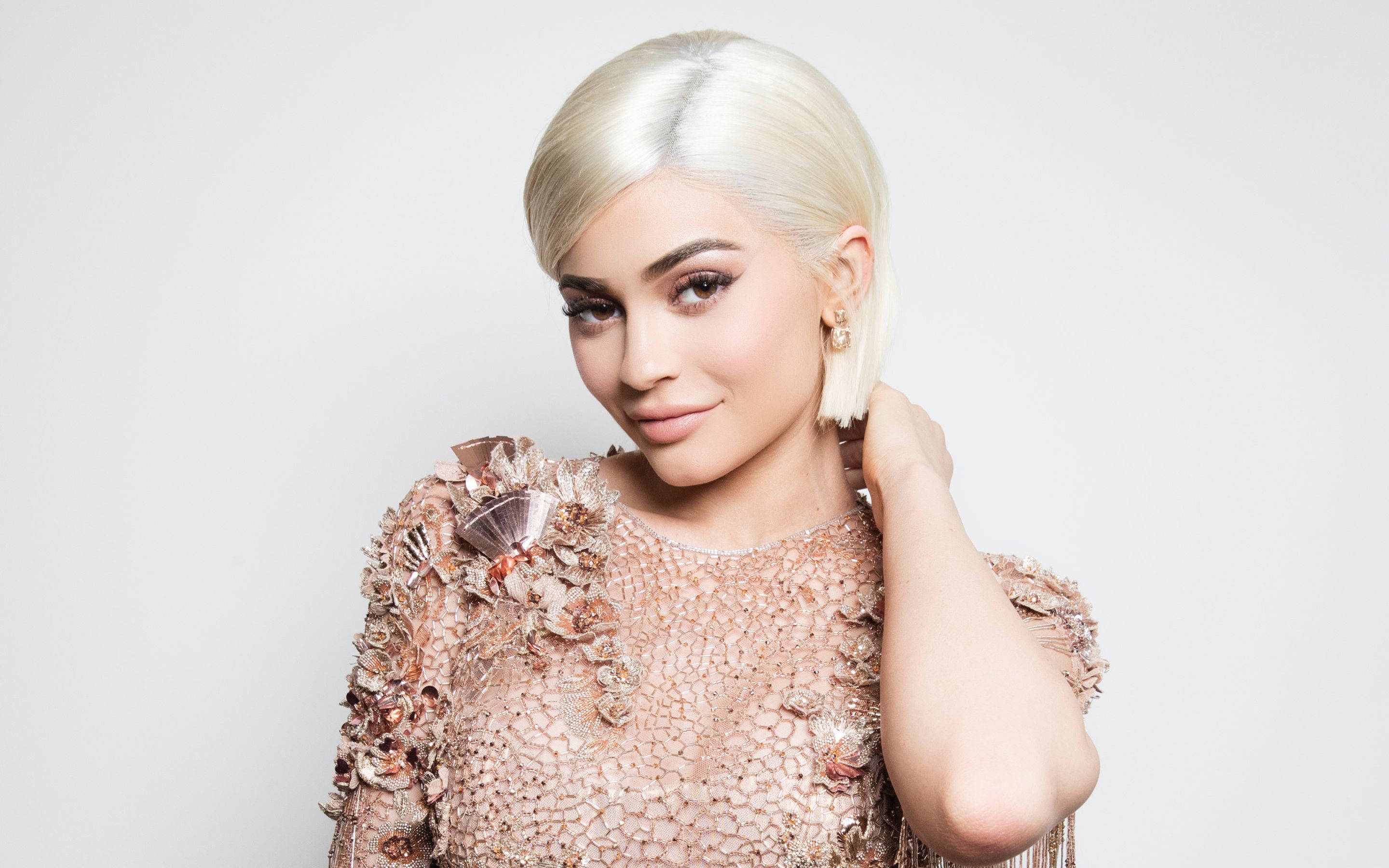 Kylie 桌布 壁紙 — 一位擁有鉑金色鮑伯頭的女性，穿著玫瑰金裝飾的禮服，背景為純白色。