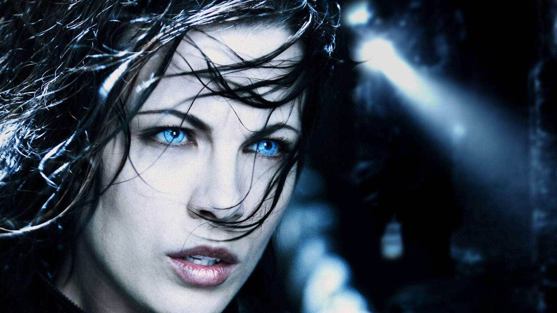 Kate Beckinsale 桌布 壁紙 — 一位擁有銳利藍眼睛和濕黑頭髮的女性，在昏暗、憂鬱的藍色環境中凝視著。