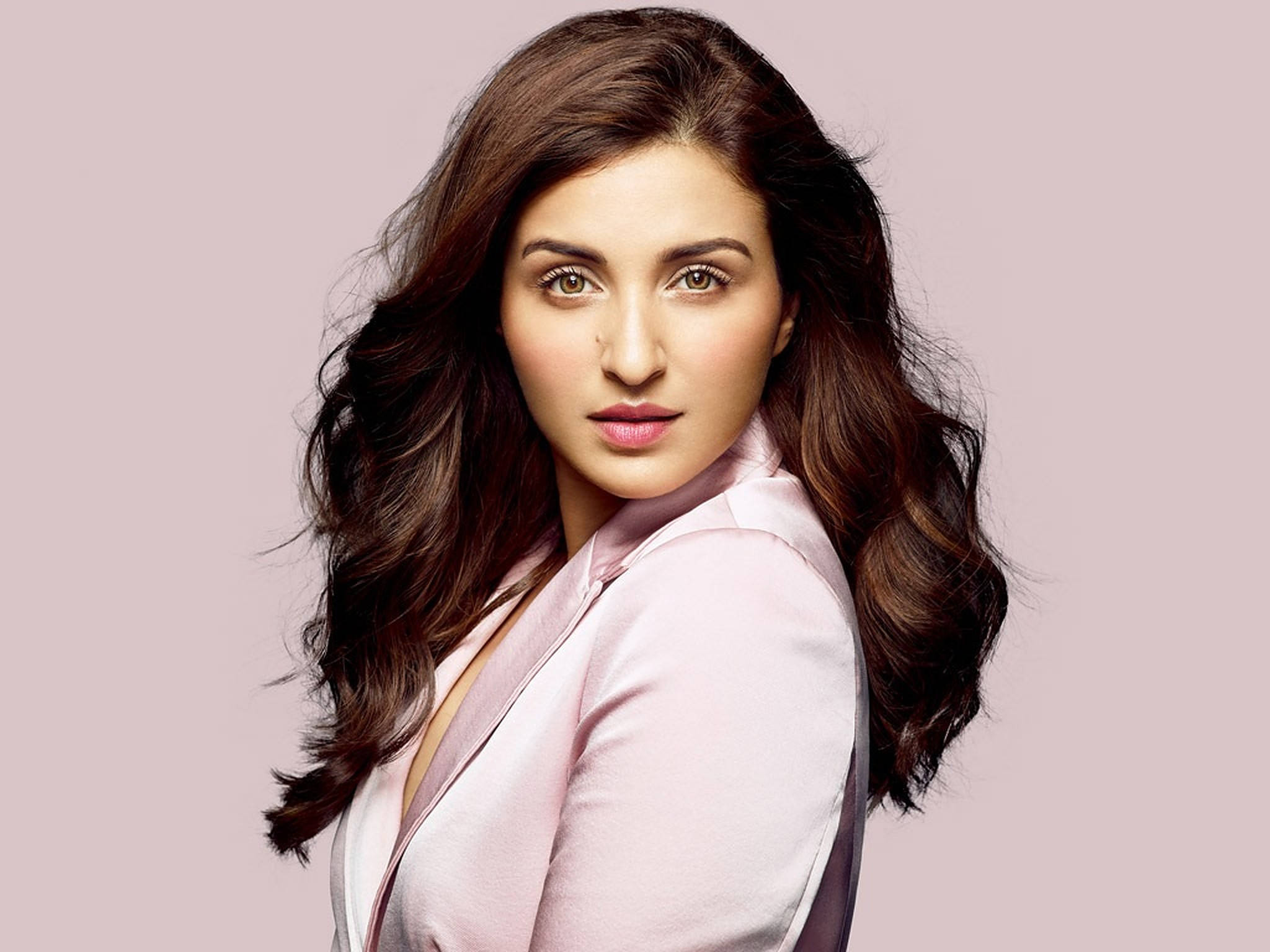 Parineeti 桌布 壁紙 — 一位擁有長波浪棕色頭髮和粉紅色西裝外套的女性，在柔和的紫紅色背景下自信地凝視。