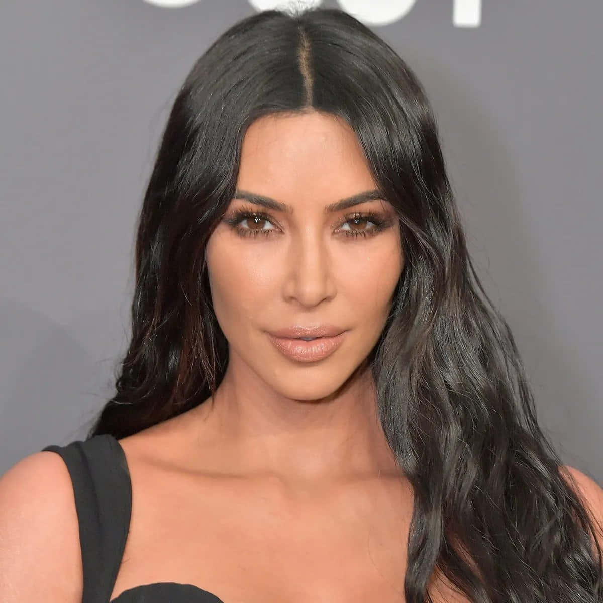 Kim Kardashian 桌布 壁紙 — 一位擁有長深色波浪髮和精緻妝容的女性特寫肖像，背景為灰色。