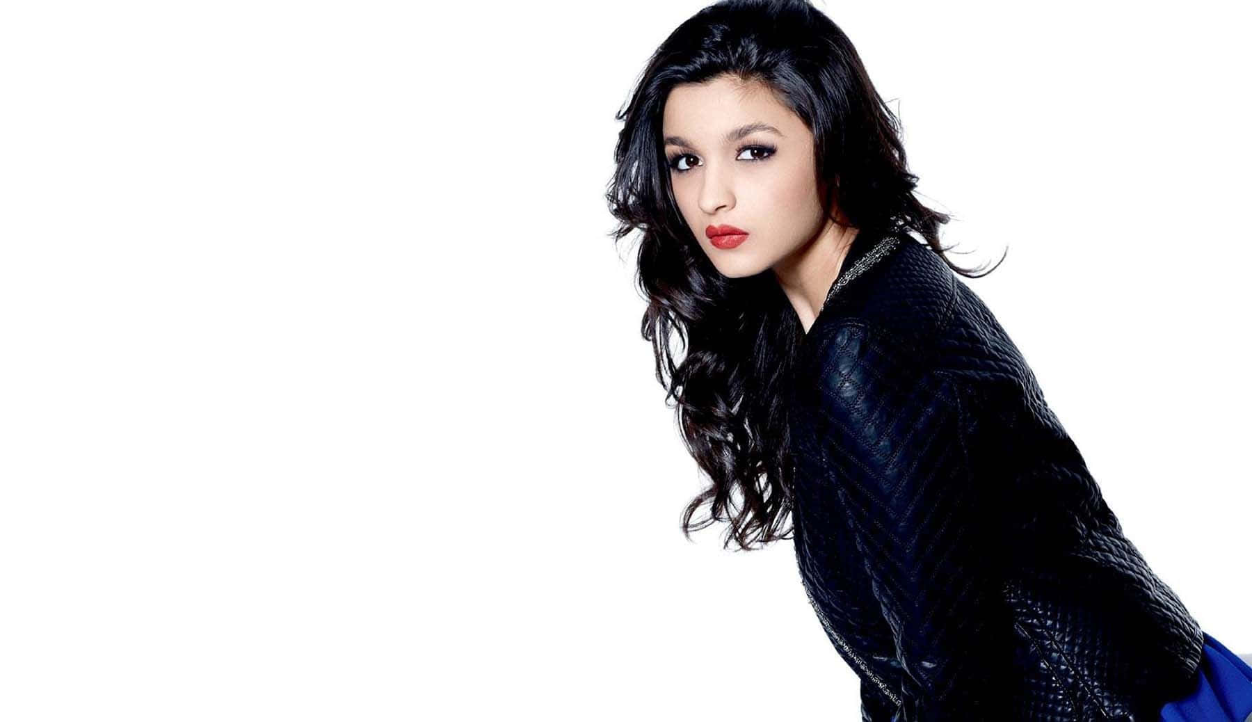 Alia Bhatt 桌布 壁紙 — 一位擁有長深色波浪髮和紅唇的女性，穿著黑色紋理外套，在純白背景前擺姿勢。