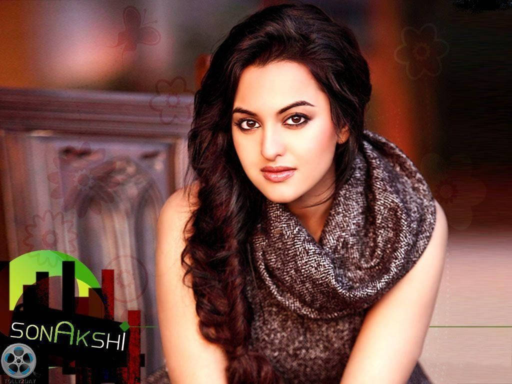 Sonakshi Sinha 桌布 壁紙 — 一位擁有長深色波浪髮和質感圍巾的女性，在柔和光線下直視鏡頭。
