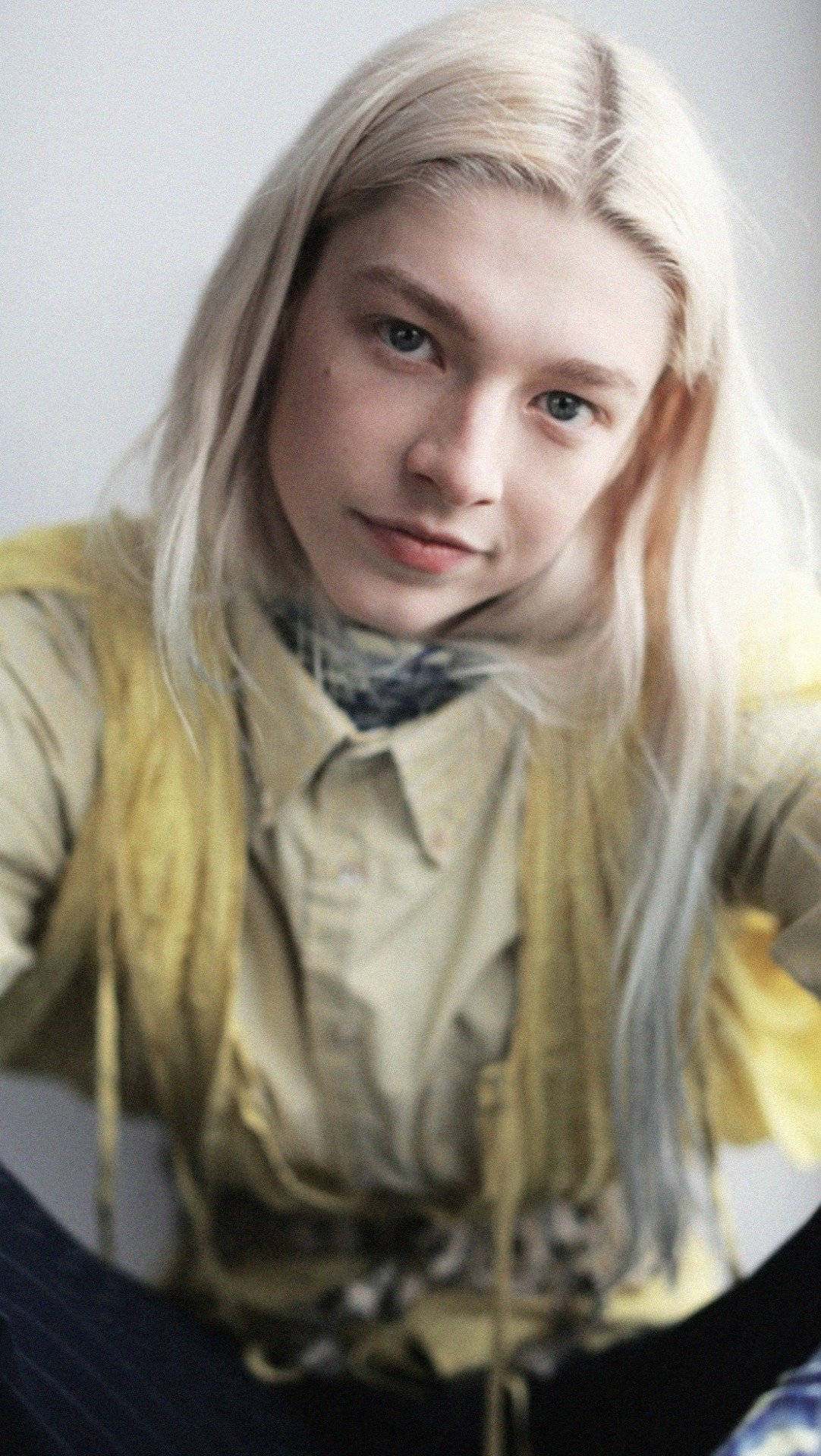 Hunter Schafer 桌布 壁紙 — 一位擁有長白金髮和藍眼睛的年輕人，穿著圖案襯衫外搭黃色背心，溫柔地凝視鏡頭。