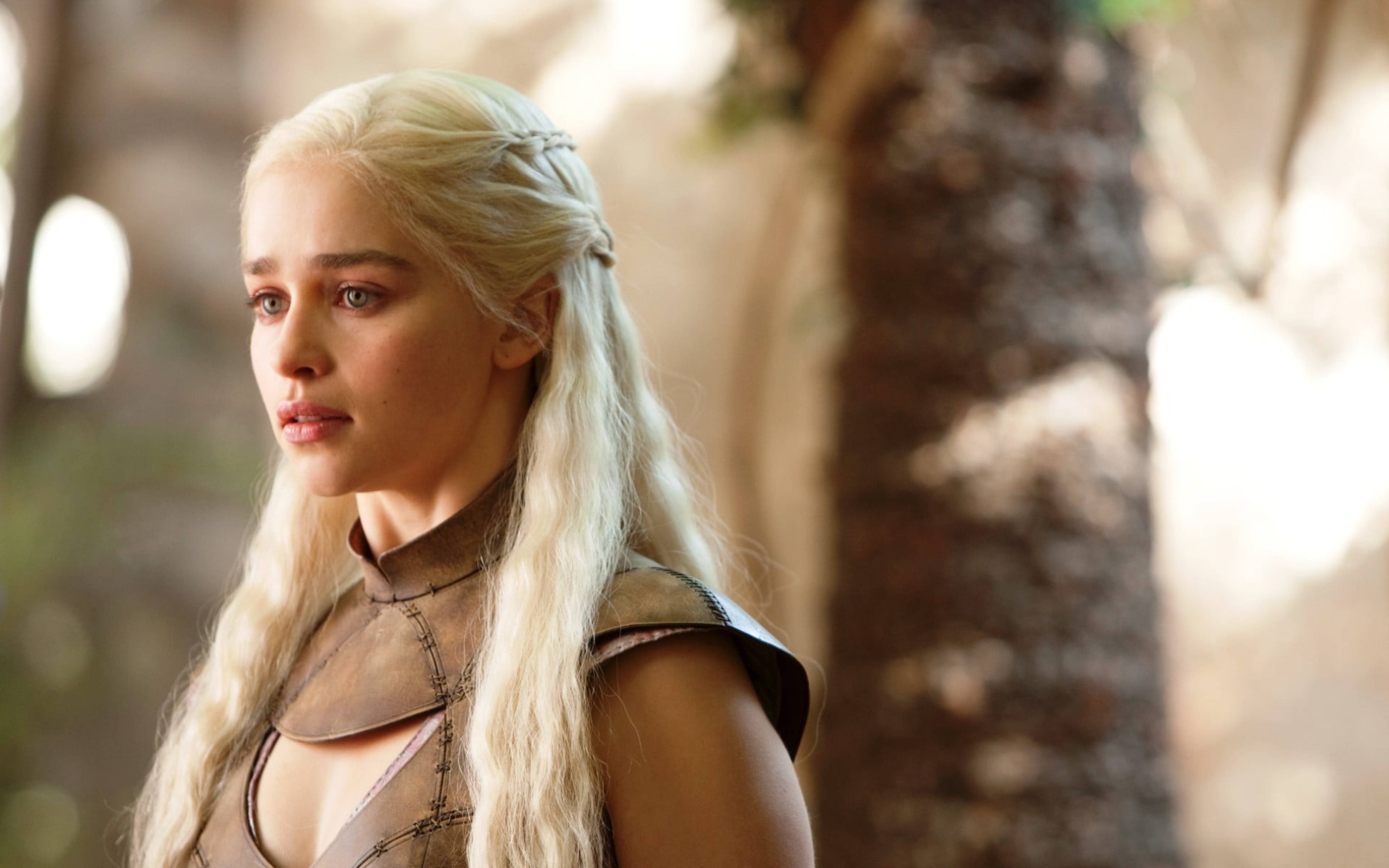 daenerys 桌布 壁紙 — 一位擁有長白金髮和銳利藍眼的女性，在陽光明媚的森林環境中若有所思地凝視。