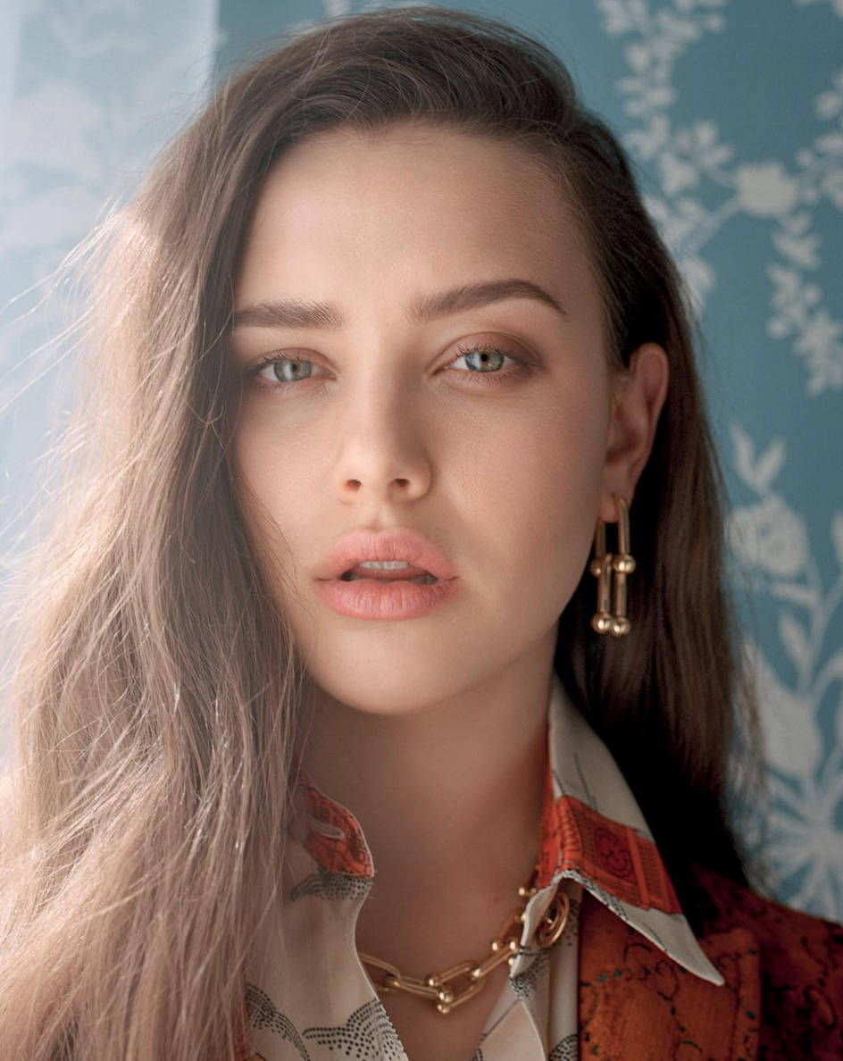 Katherine Langford 桌布 壁紙 — 一位擁有長長棕色頭髮和綠色眼睛的女性，在藍色花卉壁紙背景下溫柔地凝視。