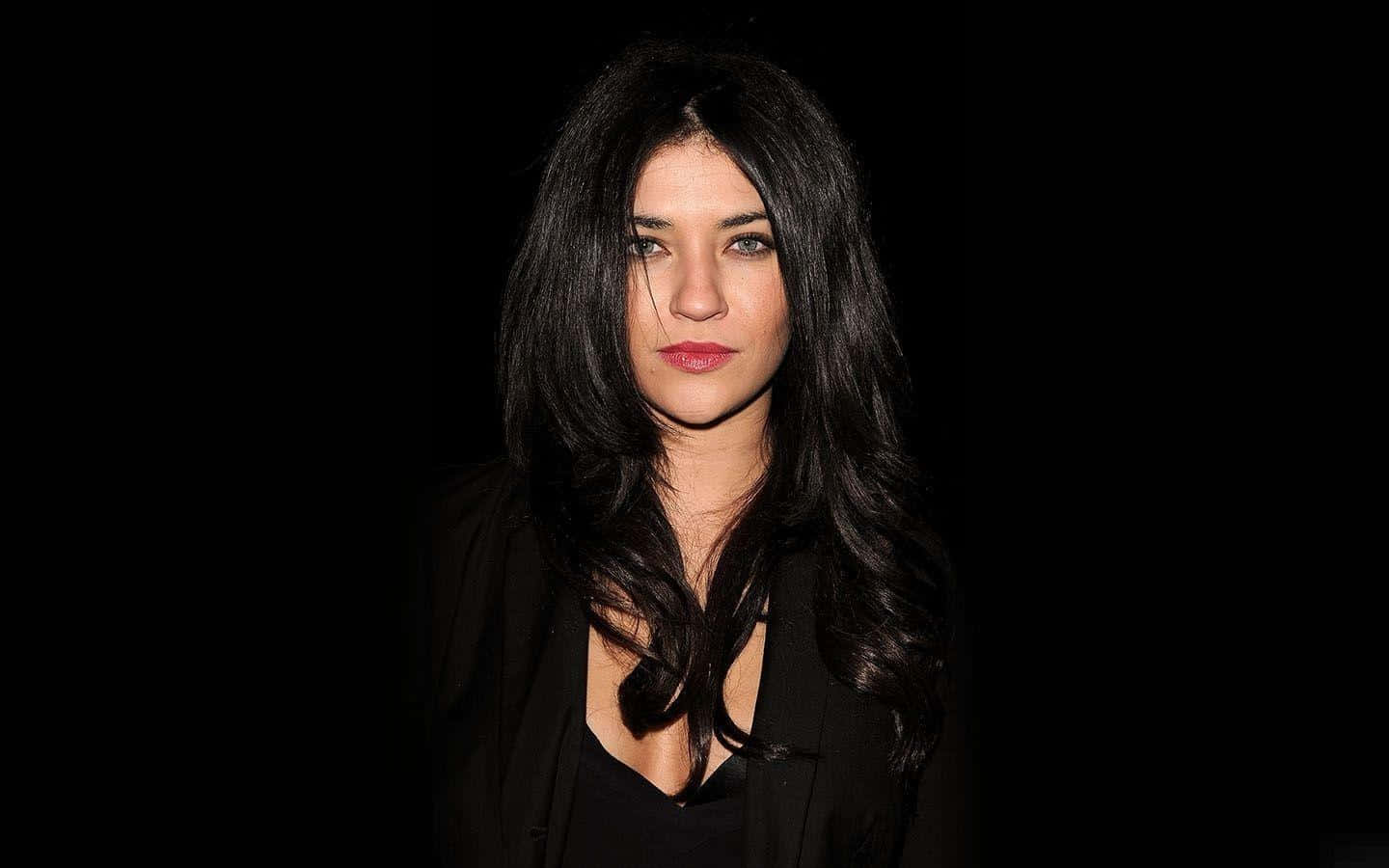 jessica szohr 桌布 壁紙 — 一位擁有長長深色頭髮和紅唇的女性，在純黑色背景下強烈凝視。