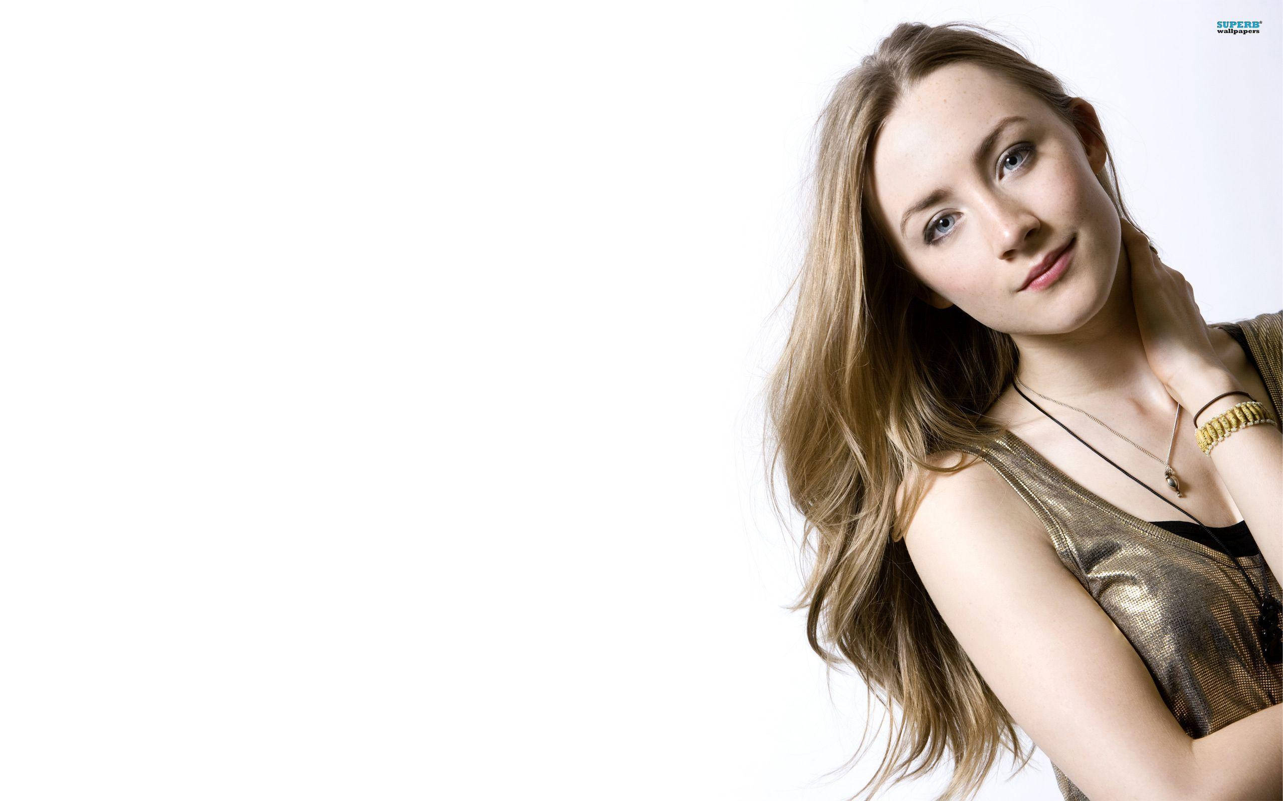 Saoirse Ronan 桌布 壁紙 — 一位擁有長長金髮和藍眼睛的女性，穿著金色上衣，在純白背景前溫柔微笑。
