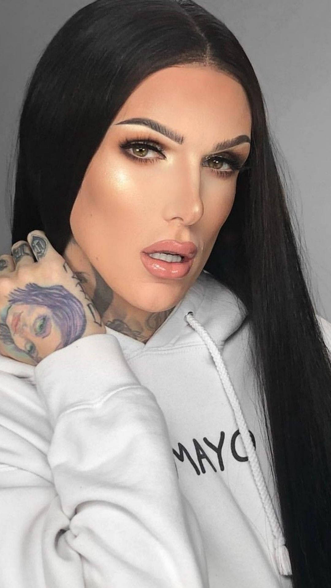 Jeffree Star 桌布 壁紙 — 一位擁有長長黑髮、頸部和手上有刺青的女性，在灰色背景前穿著白色連帽衫。