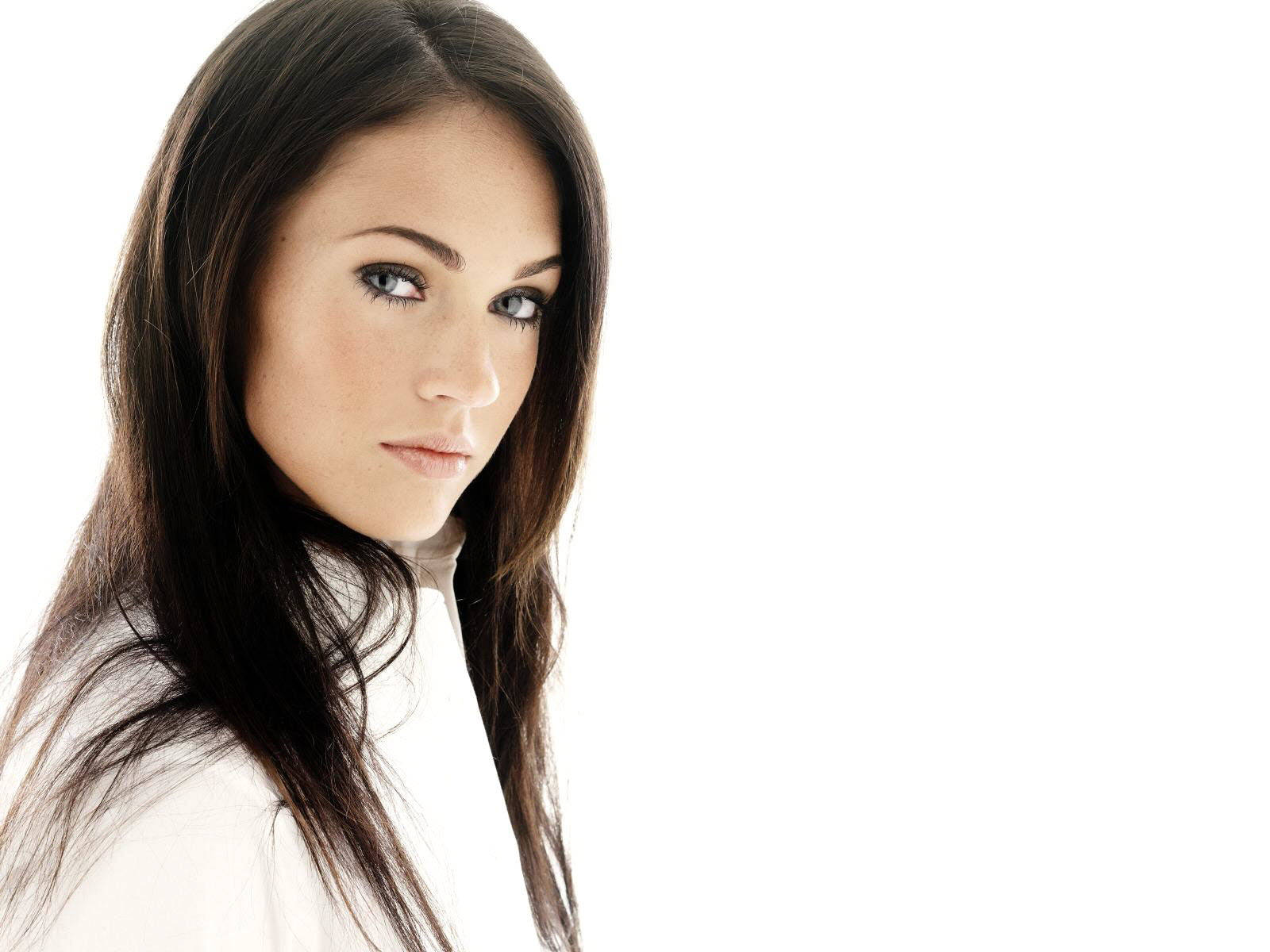 Megan Fox HD 桌布 壁紙 — 一位擁有長長黑髮和引人注目的藍眼睛的女性，在純白背景下直視鏡頭。