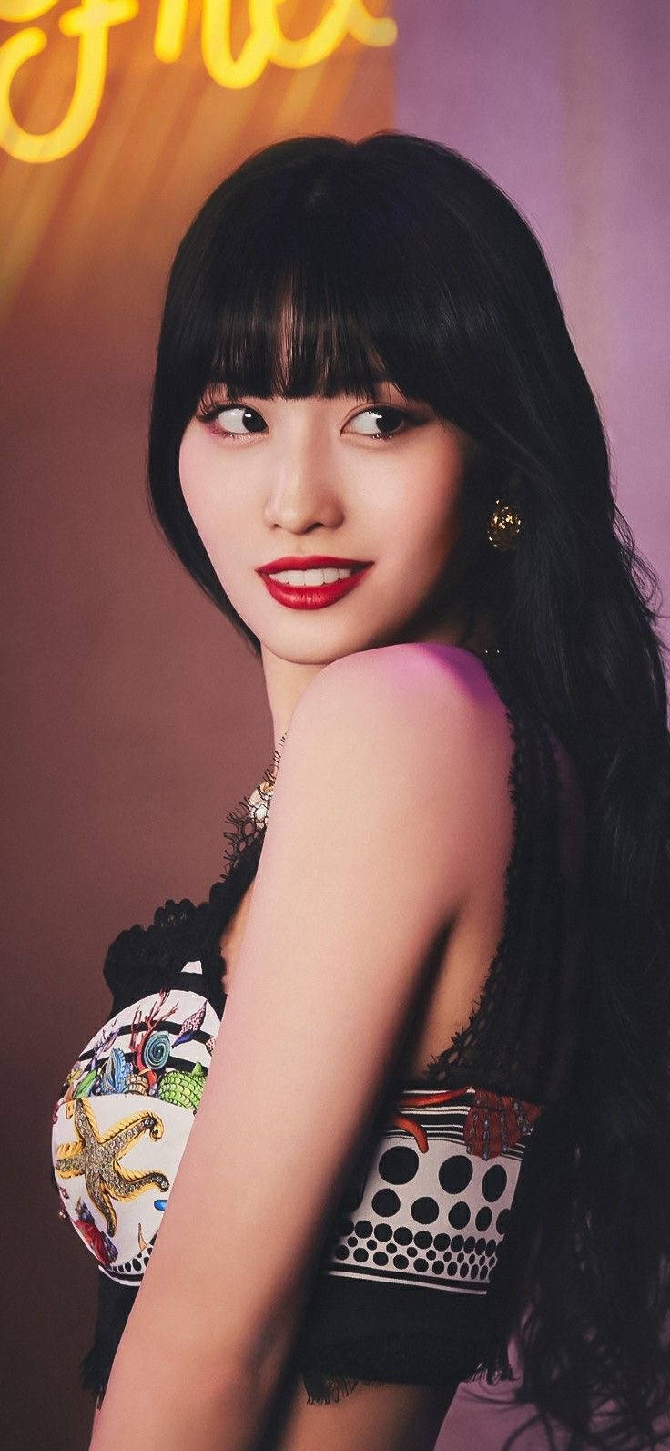 Momo 桌布 壁紙 — 一位擁有長黑髮和紅唇的女性，穿著圖案上衣，在溫暖的霓虹燈背景下擺姿勢。