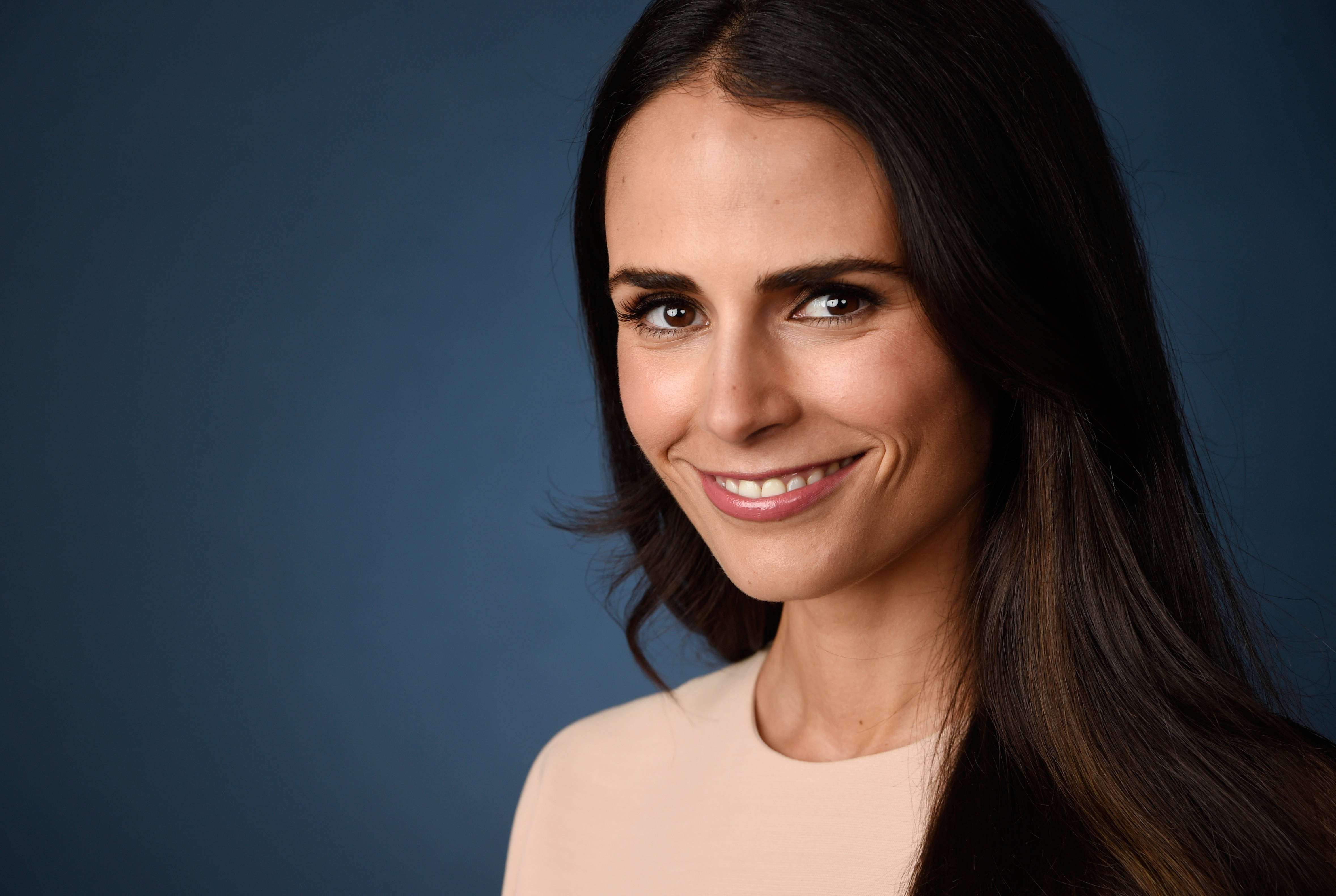 Jordana Brewster 桌布 壁紙 — 一位擁有長黑髮的女性在純藍色攝影棚背景前溫暖地微笑。