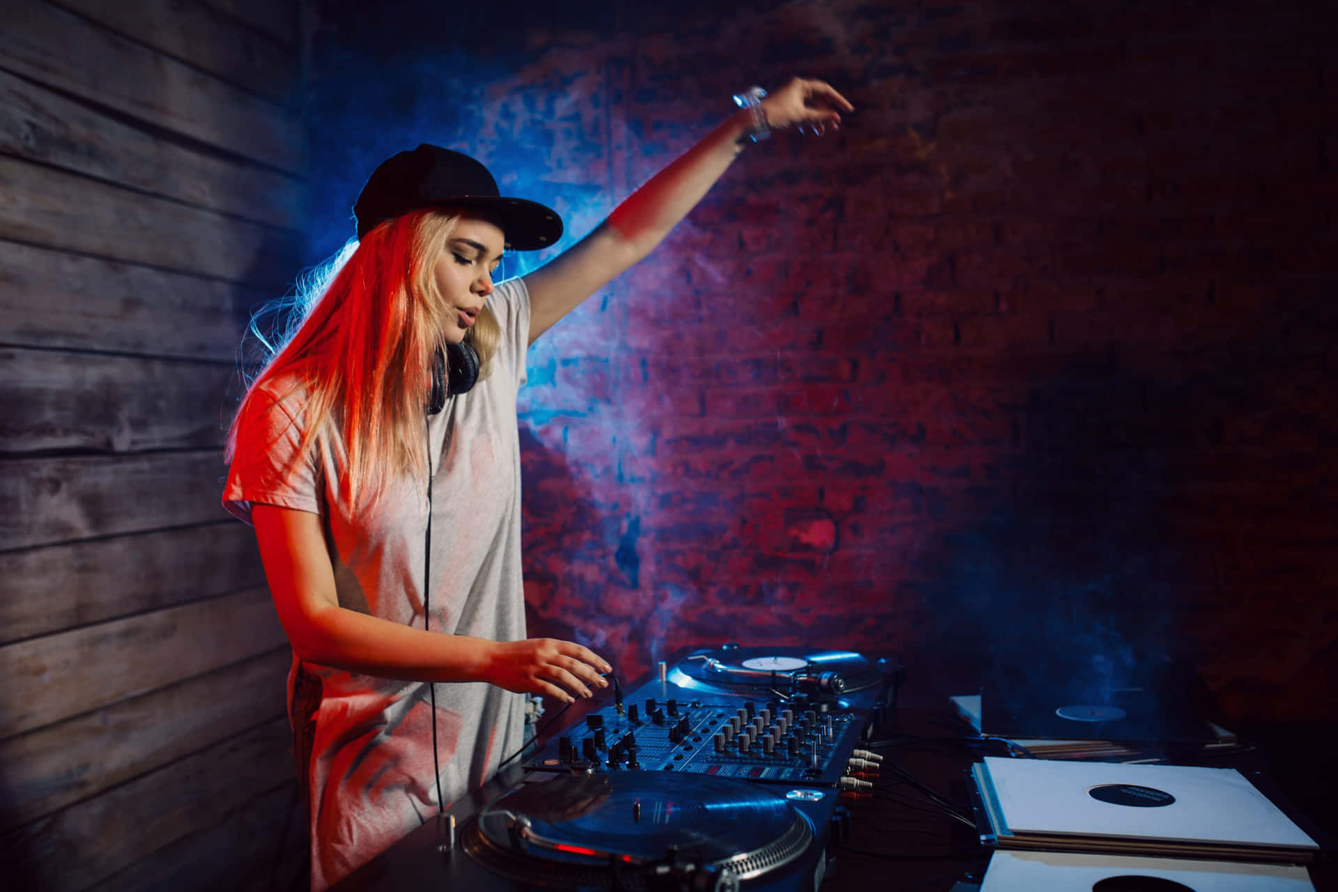 DJ 桌布 壁紙 — 一位擁有閃亮紅髮的女DJ在霓虹燈下，於煙霧瀰漫的磚牆俱樂部中用唱盤混音。